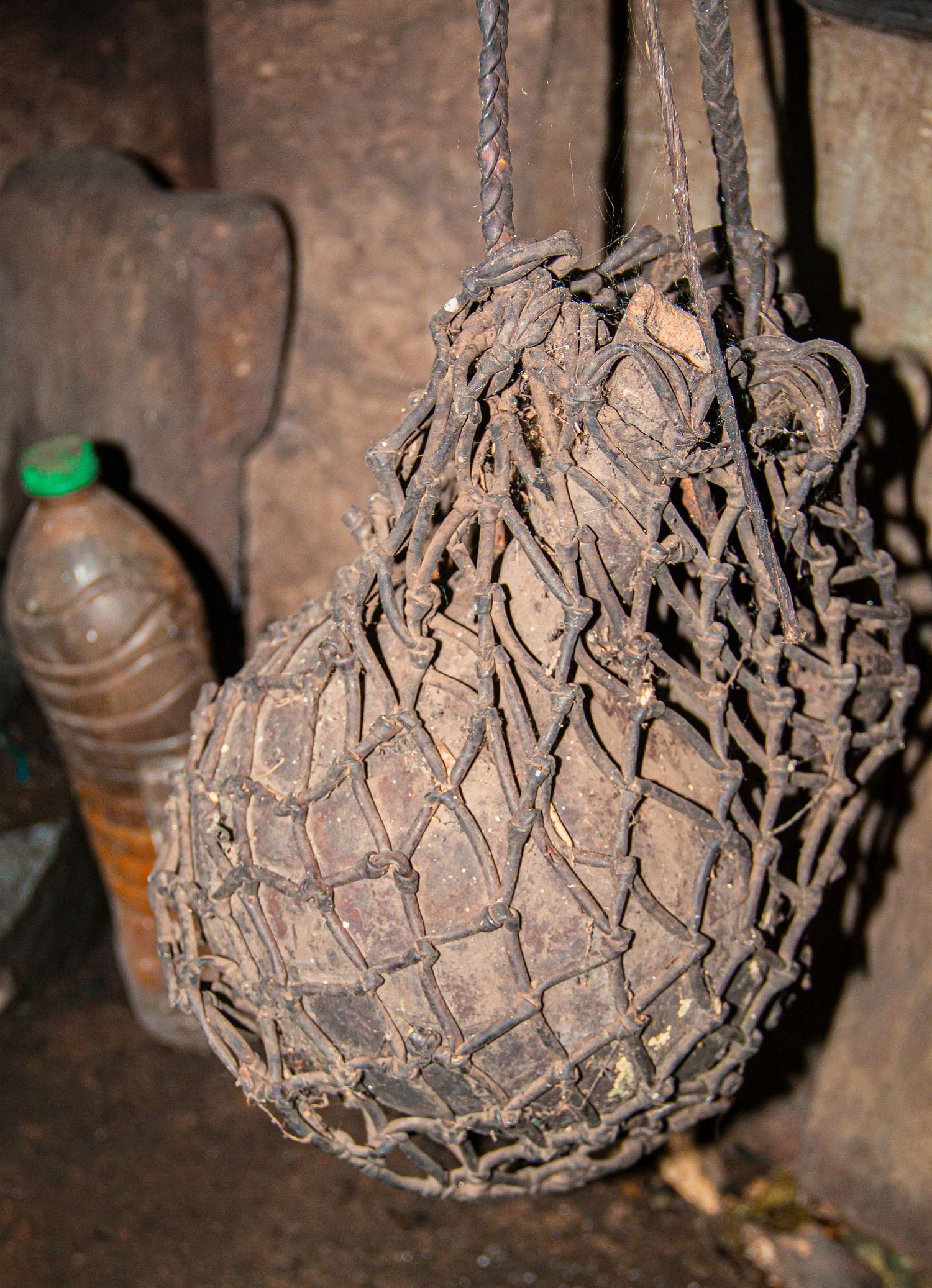 Ancient dried gourd wrapped in a handwoven rope net hanging in a rustic traditional African setting.