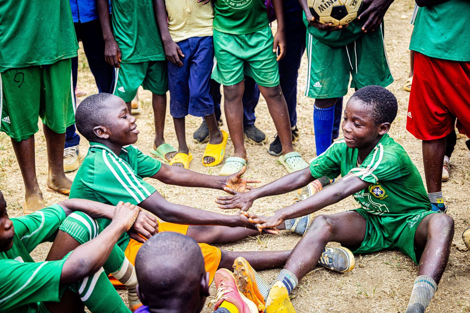 African children in green soccer uniforms playing and laughing together on a dirt field.