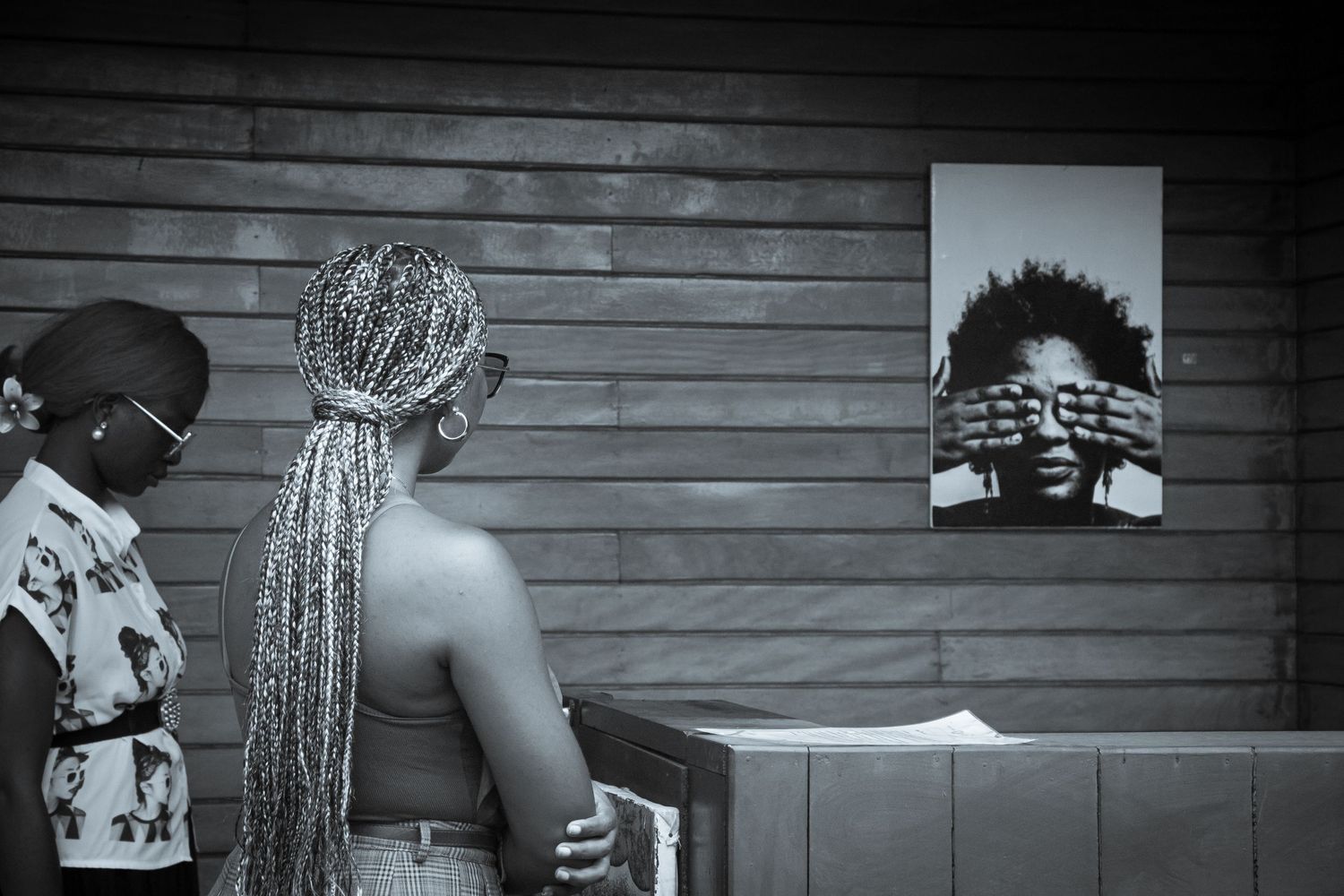 Black and white photo of two women admiring a portrait photograph displayed on a wooden wall.
