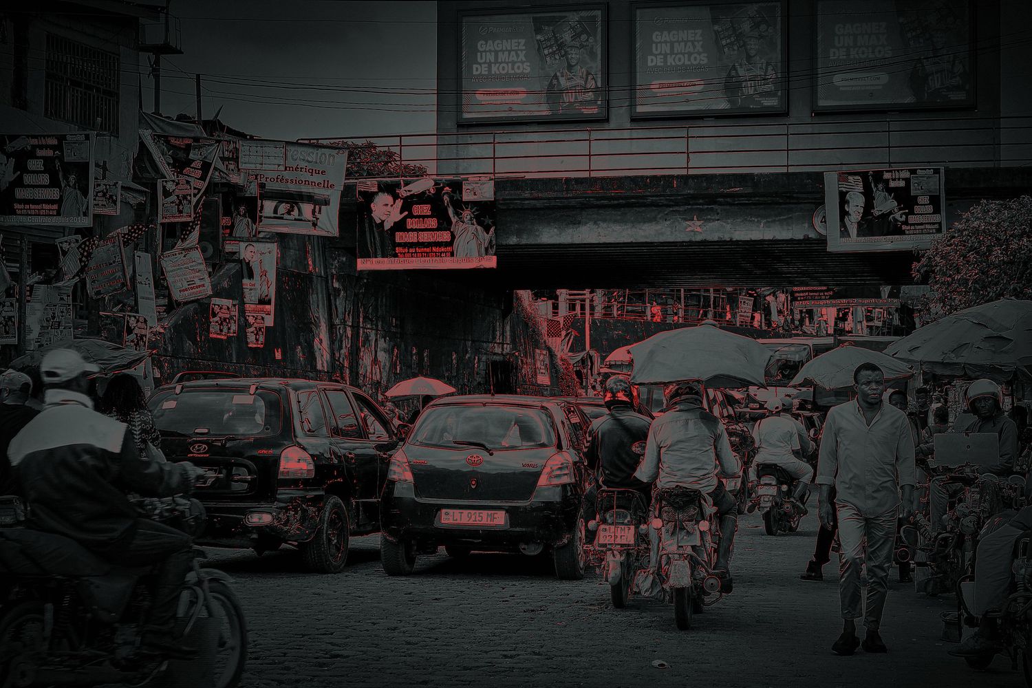 Busy African street market with heavy traffic, colorful billboards, and crowds of people in an urban setting.