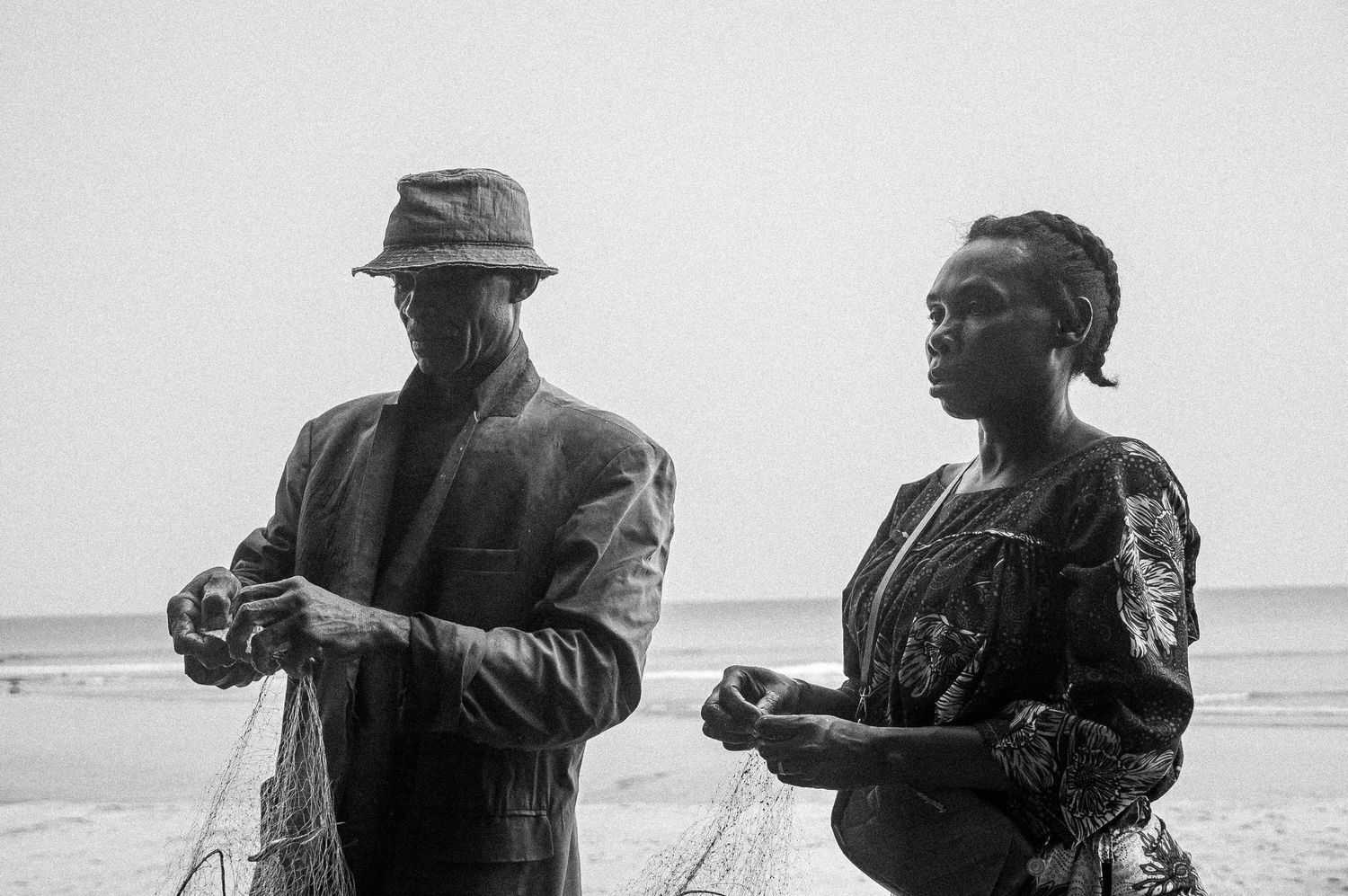 Black and white photo of two people standing on a beach with fishing nets.