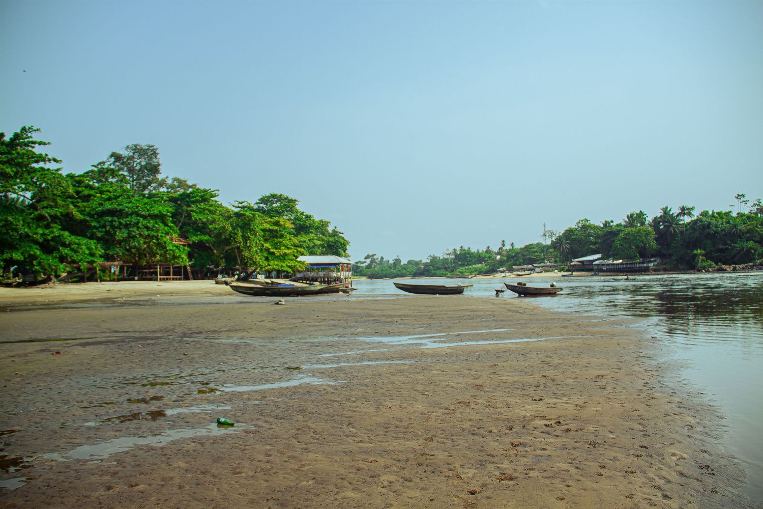 Tranquil tropical beach with wooden fishing boats resting on sandy shore lined with lush trees.