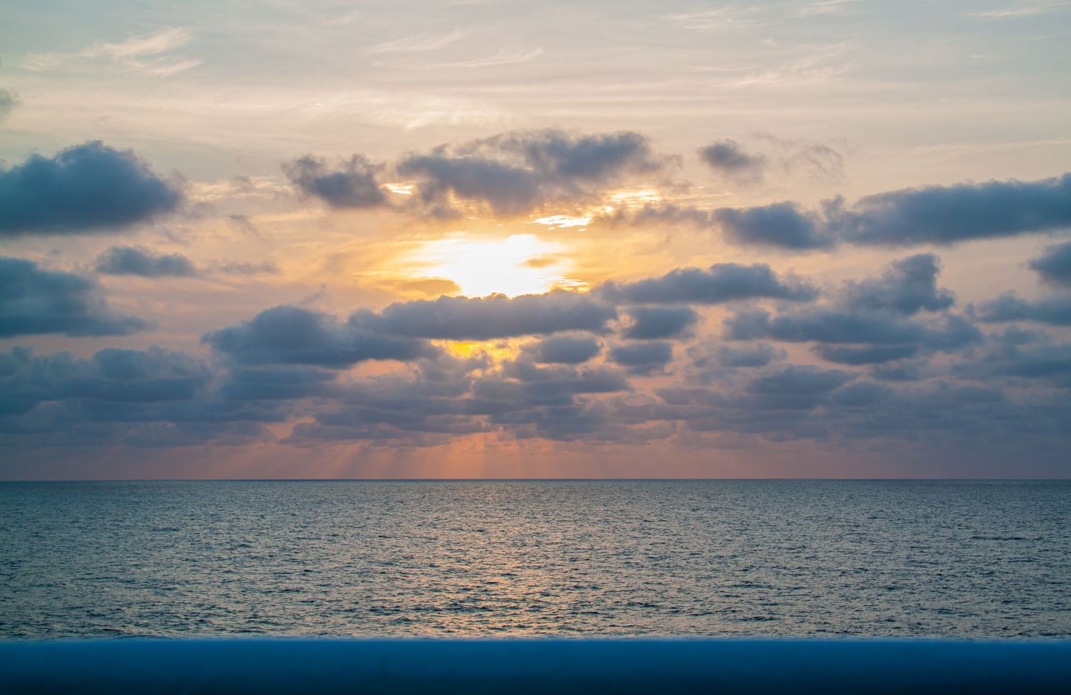 Stunning ocean sunset with dramatic clouds and golden sunrays reflecting on calm blue sea waters.