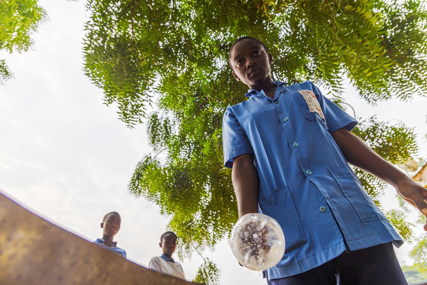 Low angle view of African student in blue uniform holding a ball under green trees.