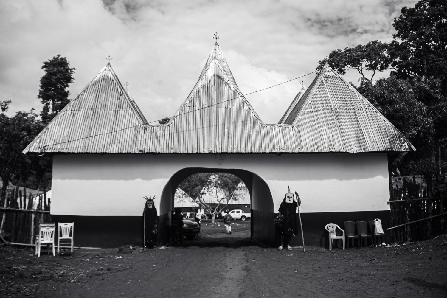 Black and white photo of traditional African thatched roof entrance gate with two figures standing guard.
