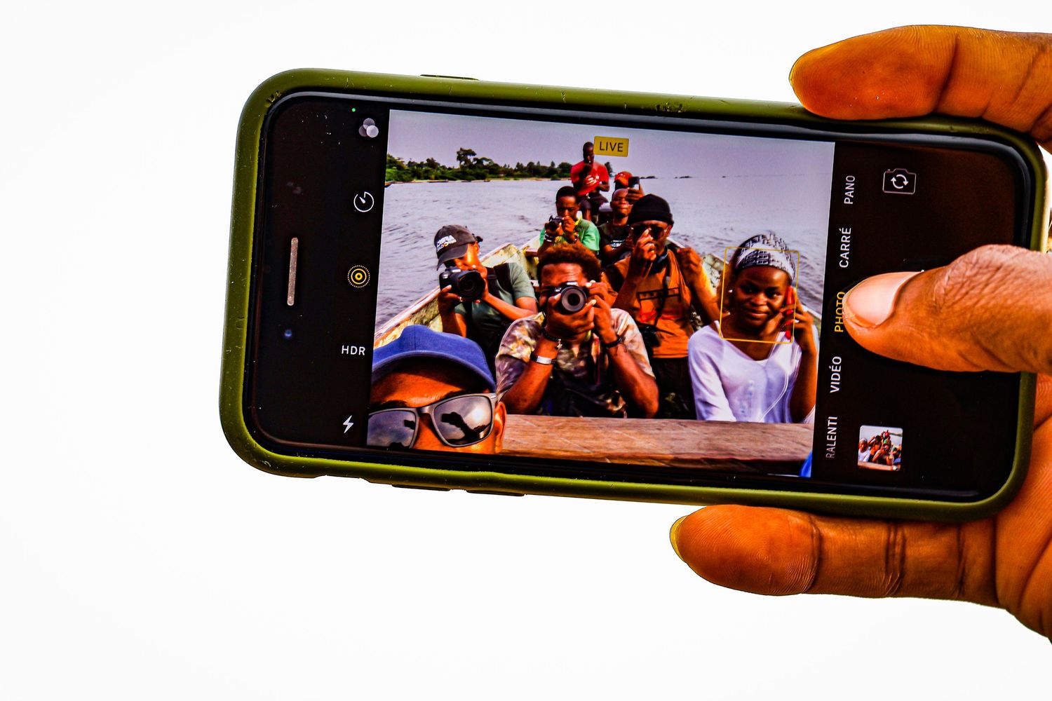 A hand holds a smartphone displaying a selfie of a group of people riding together on a river boat.