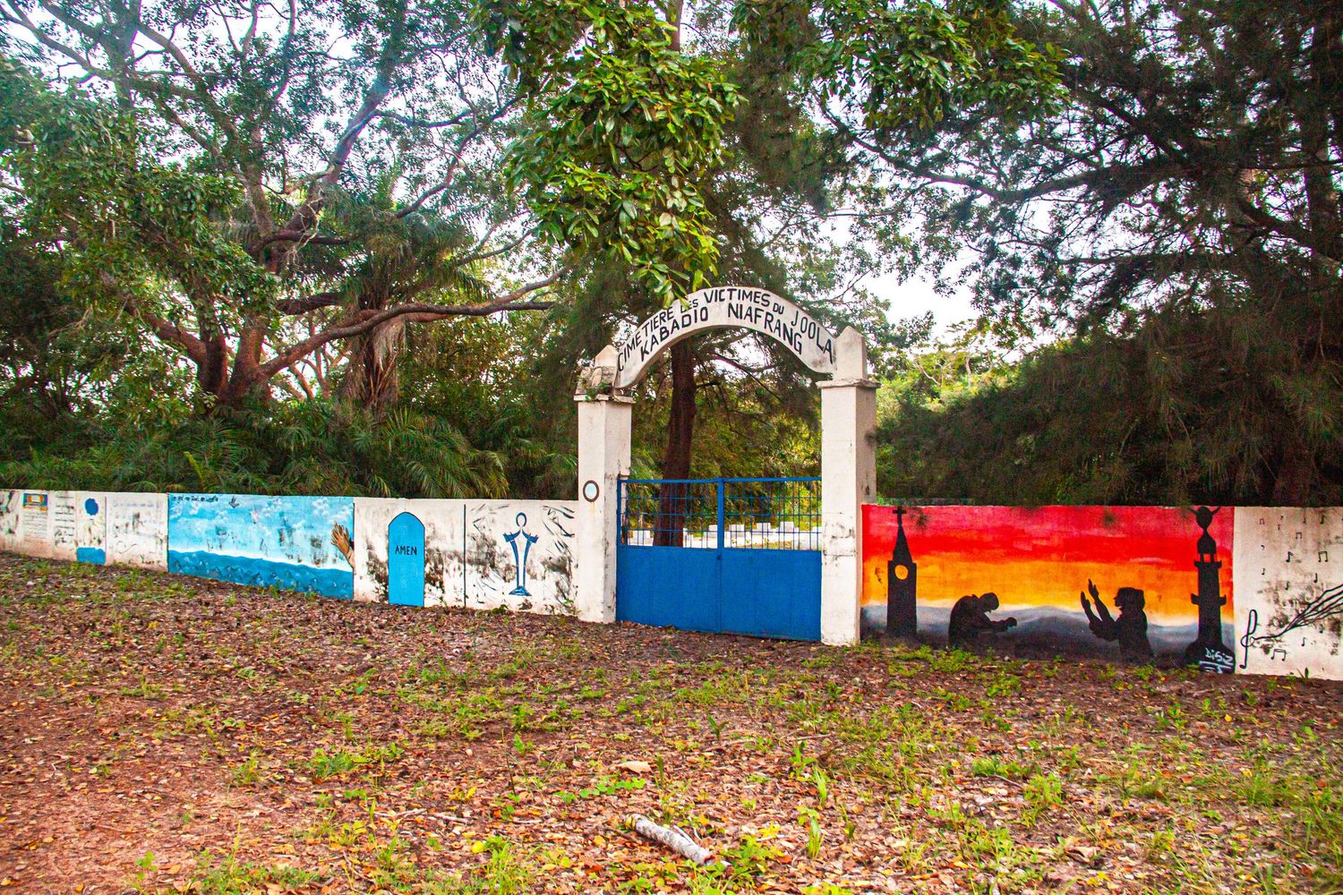 Colorful mural-decorated gate entrance surrounded by tropical trees in Senegal.