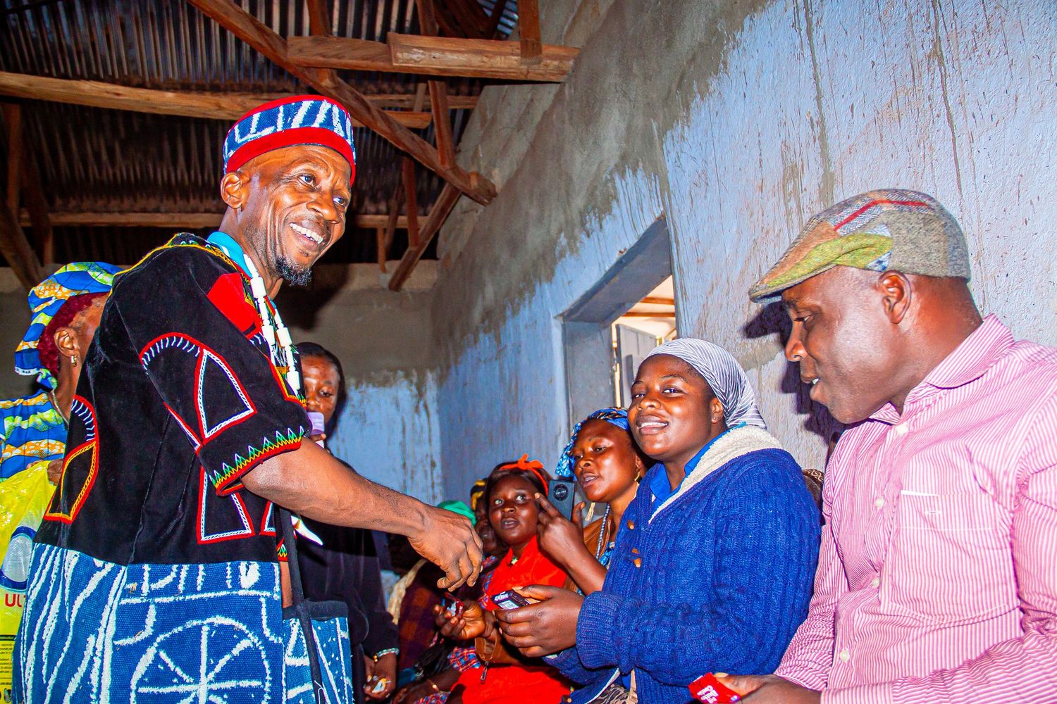 African chief in traditional embroidered attire greeting community members at a cultural gathering.