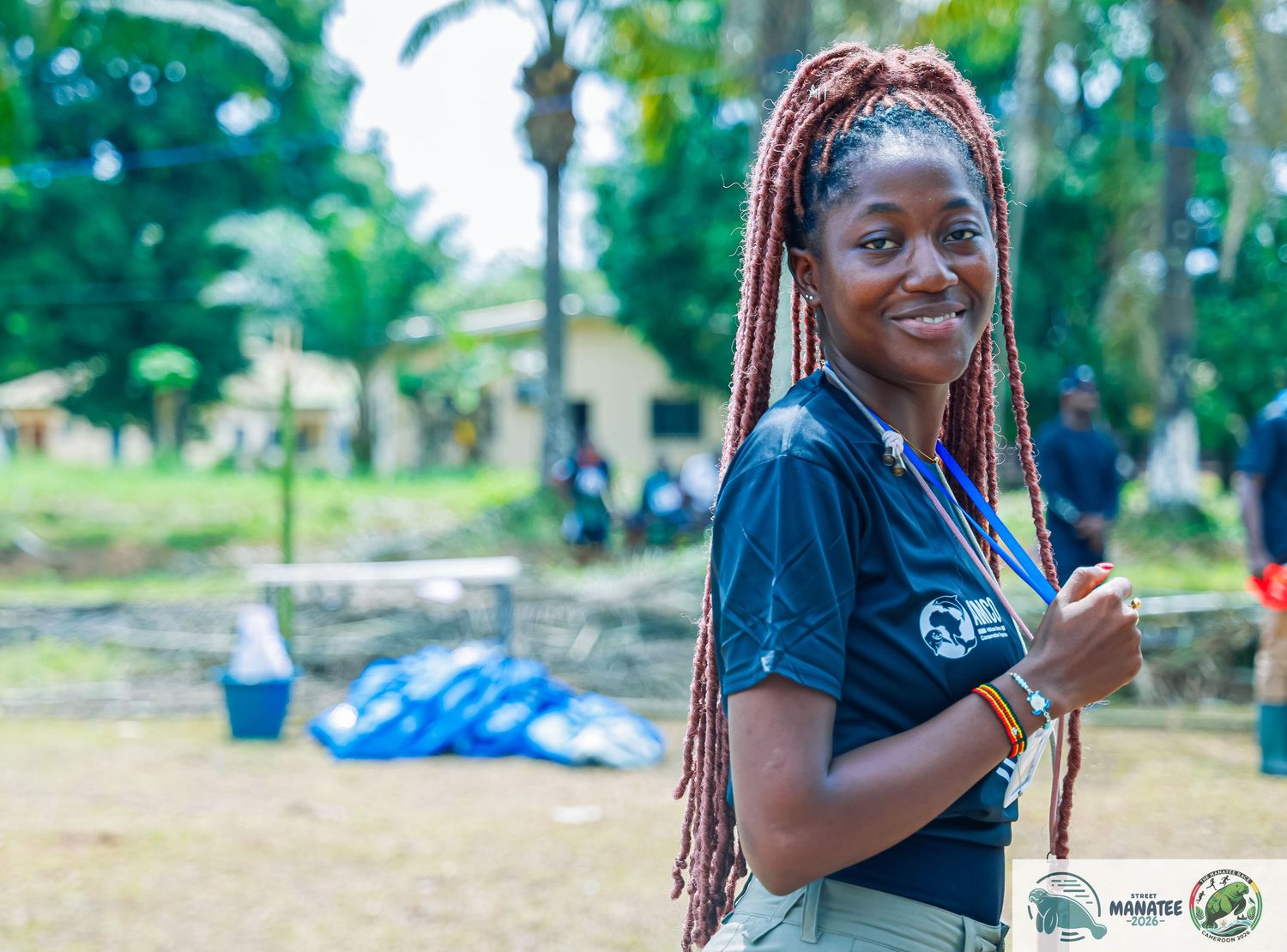 Smiling woman with red braids wearing blue event staff shirt outdoors.