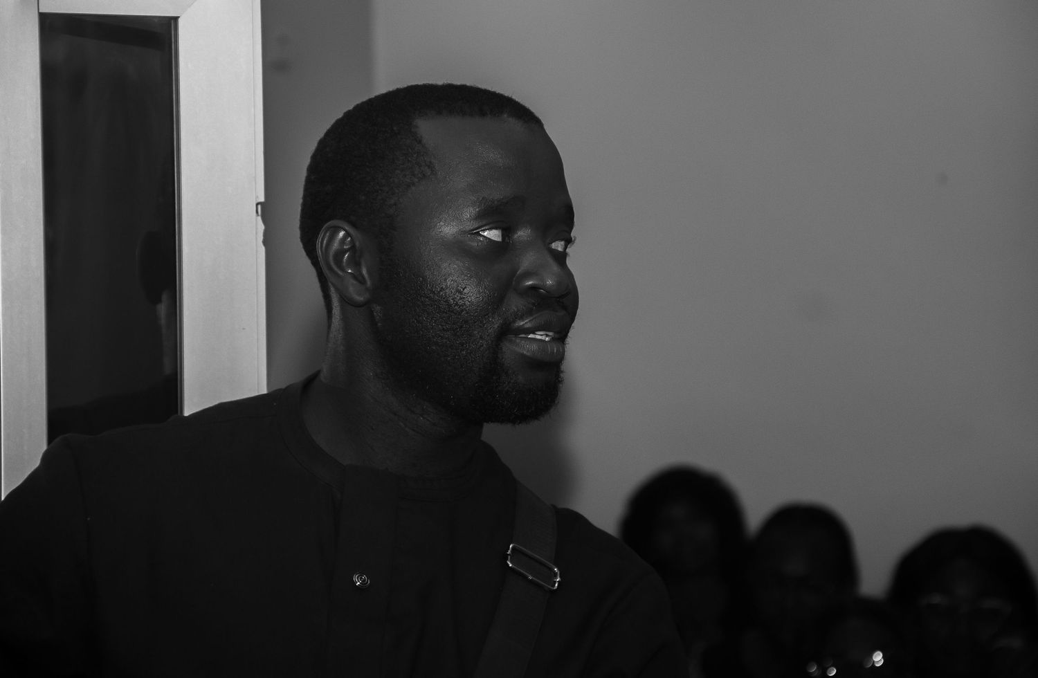 Black and white profile portrait of a tall African man in a dark shirt indoors.
