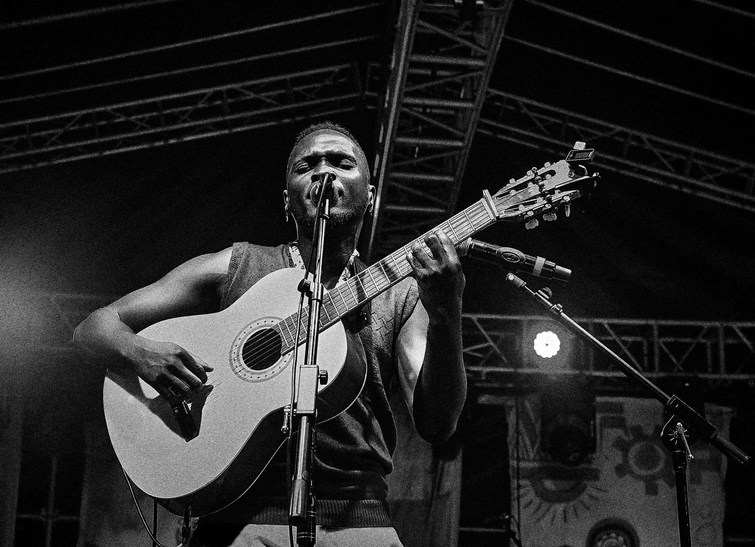Black and white photo of a young African musician performing acoustic guitar on stage at an outdoor concert.
