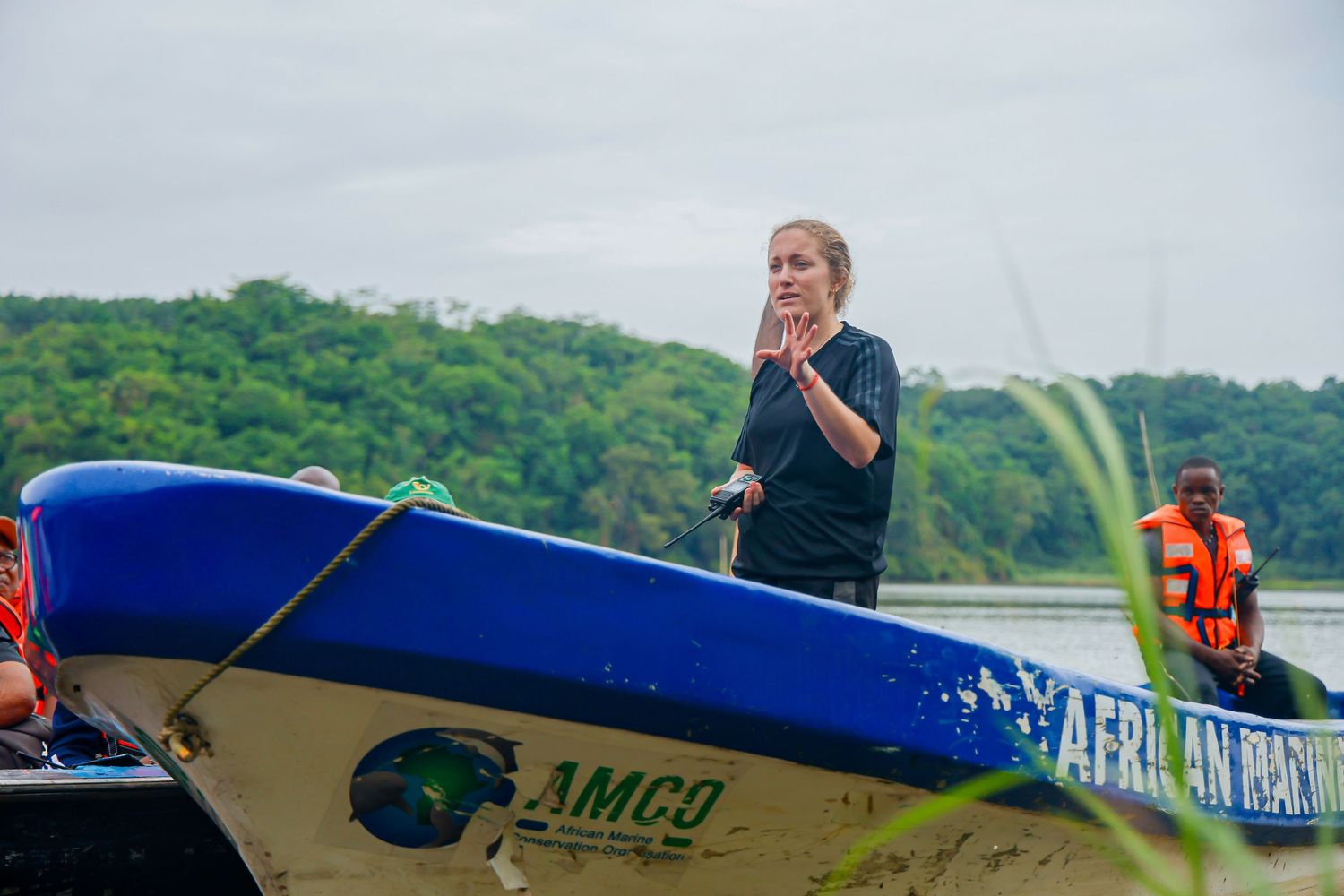 Woman standing on a boat labeled African Man on a river with lush hills.
