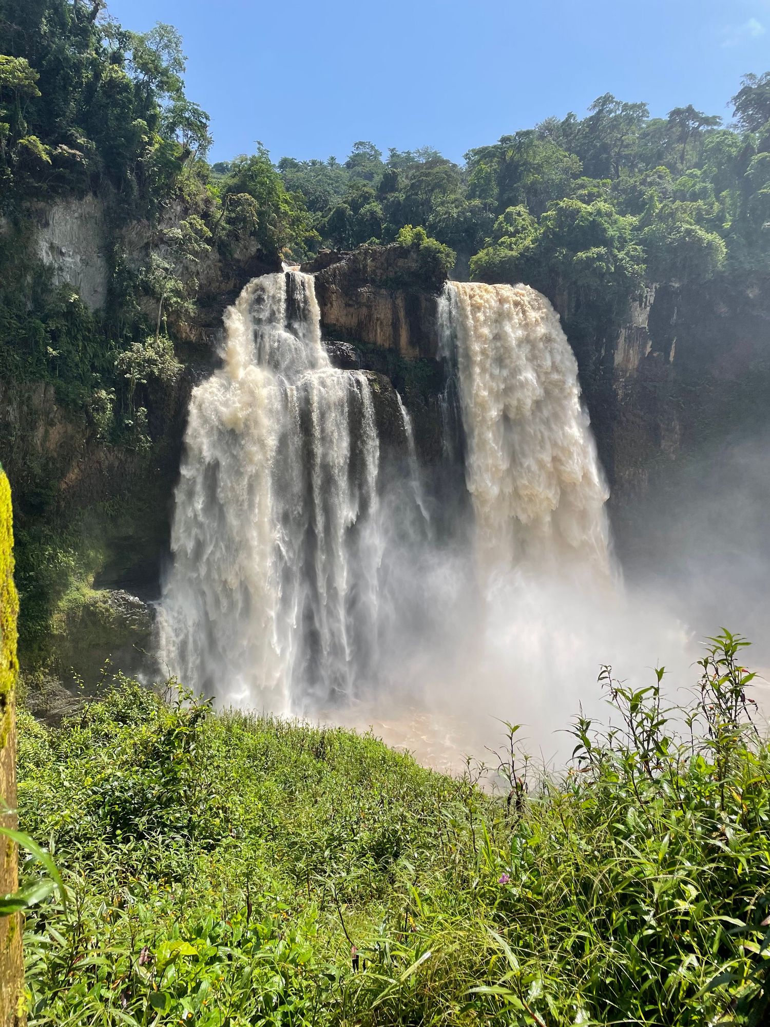 Majestic double waterfall crashing through verdant jungle landscape under a clear blue sky.