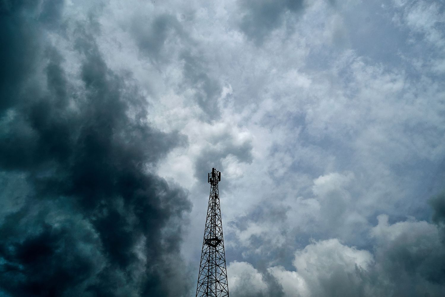 Tall communication tower against dramatic stormy dark cloudy sky.