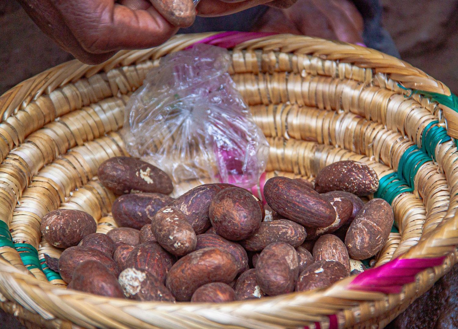 Fresh kola nuts displayed in a woven straw basket with a plastic bag at an African market.