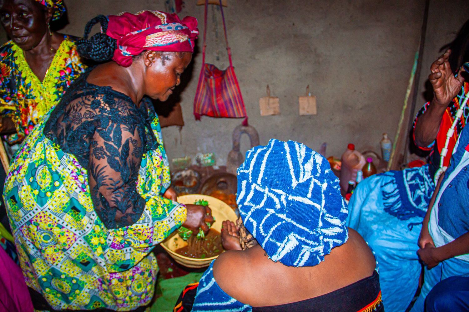 African women in colorful traditional attire gathered indoors sharing a meal during a cultural ceremony.