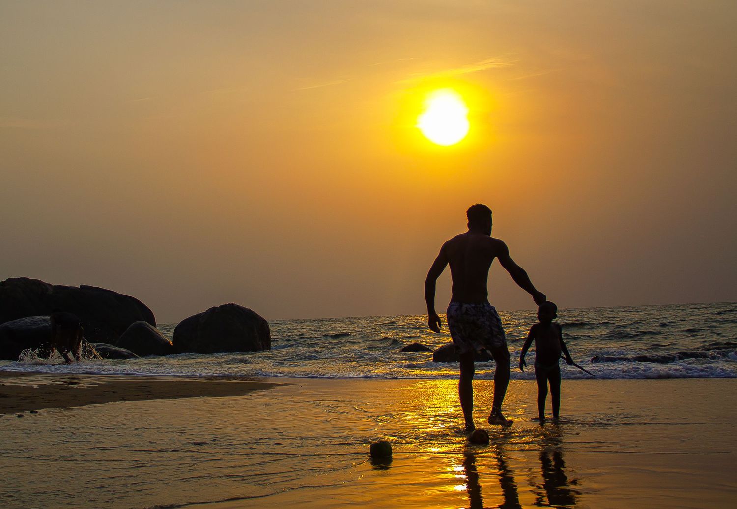Silhouette of a person and child playing on a beach during a golden sunset over the ocean.
