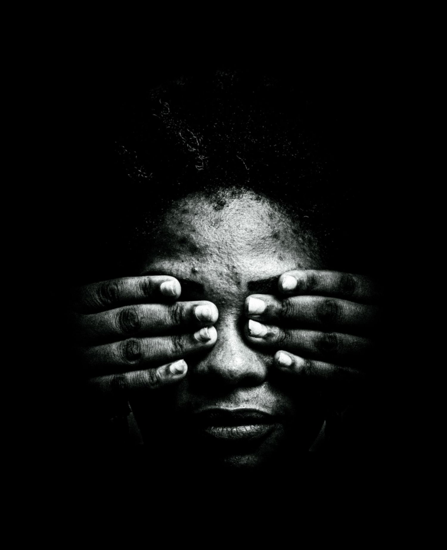 Dramatic black and white portrait of person covering face with both hands in darkness.