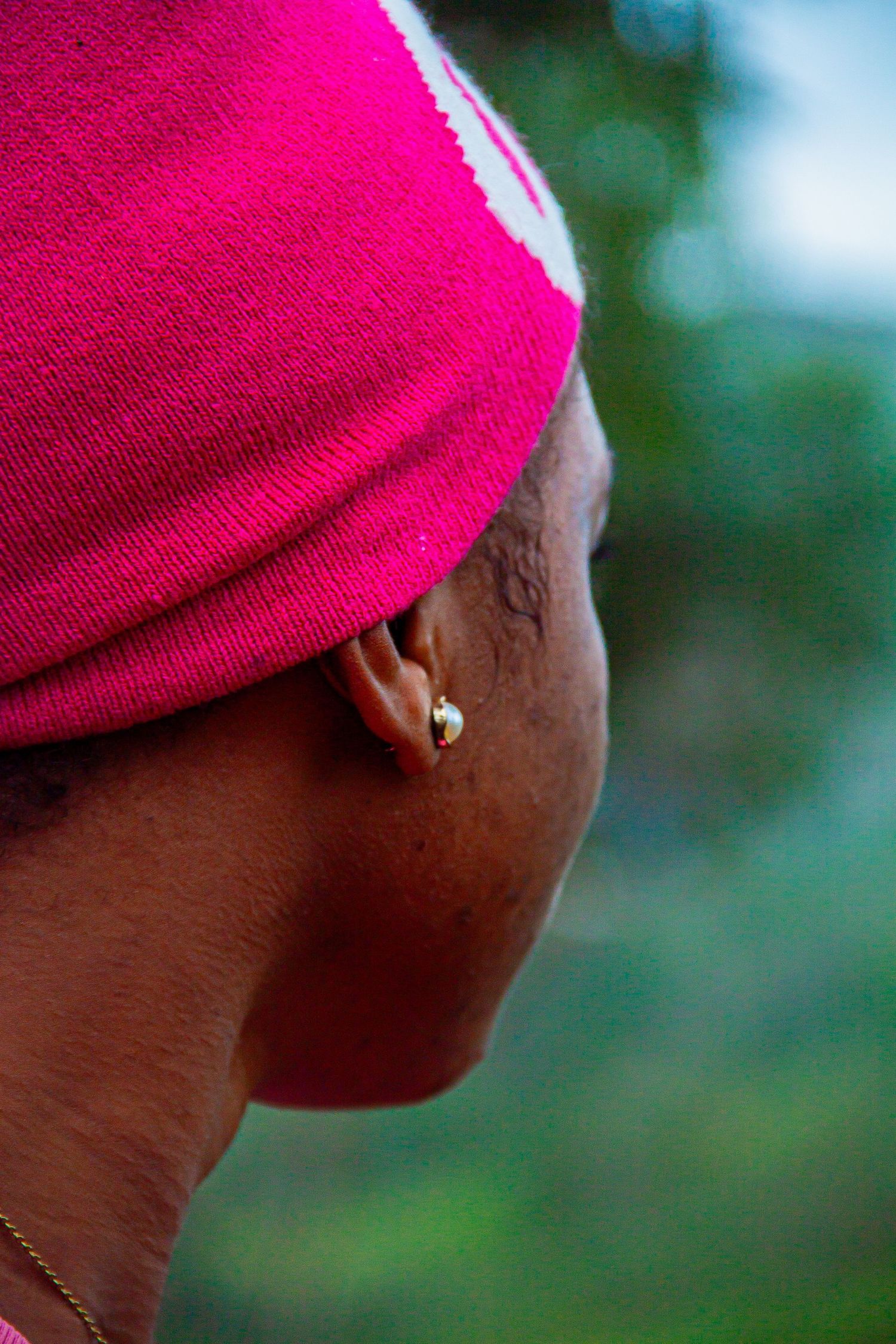 Close-up side profile of a person wearing a pink head wrap and small gold earring outdoors.