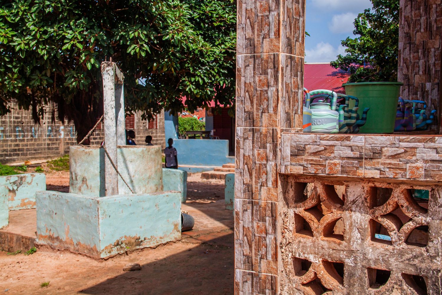 A traditional water well beside decorative brick lattice wall in a colorful West African courtyard.