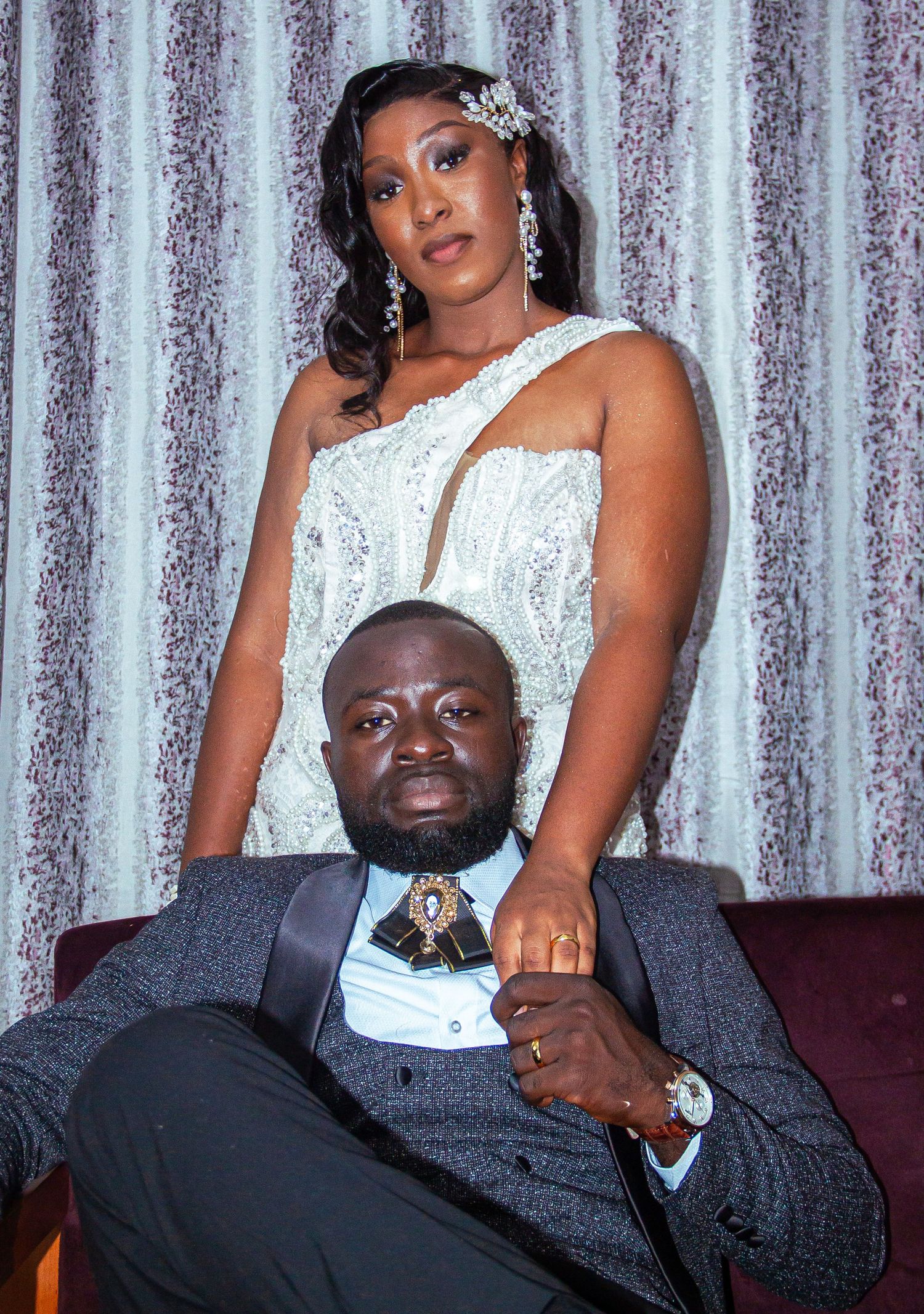 Elegant couple posing together, woman in white beaded gown and man in gray tuxedo.