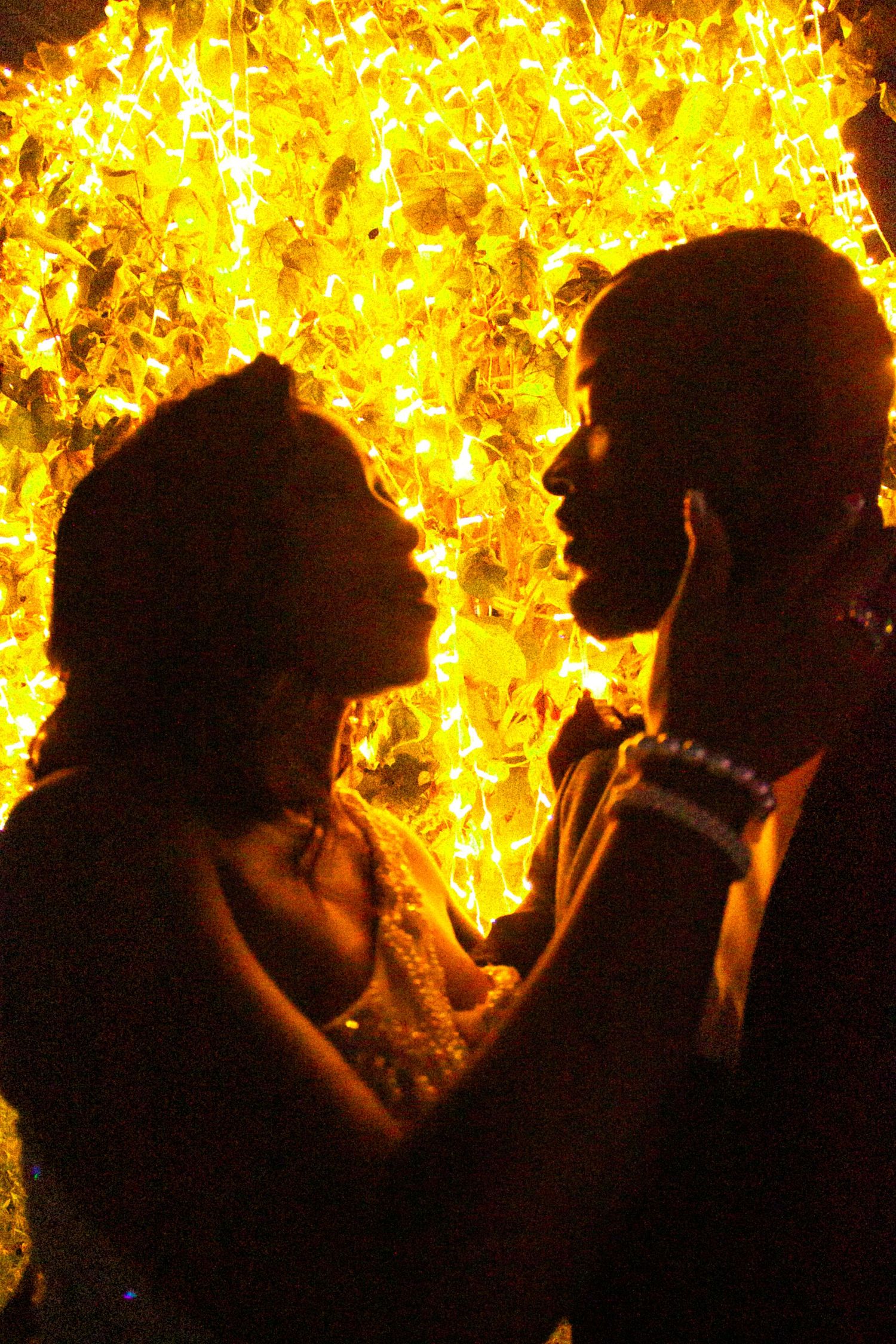 Romantic couple silhouette facing each other against glowing golden heart light display.