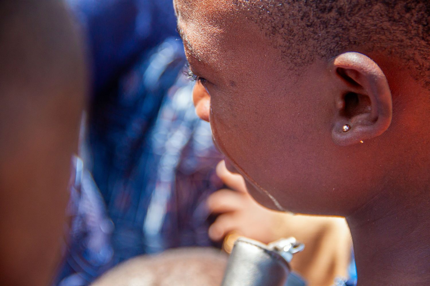 Close-up portrait of young African child drinking from metal cup in bright sunlight.