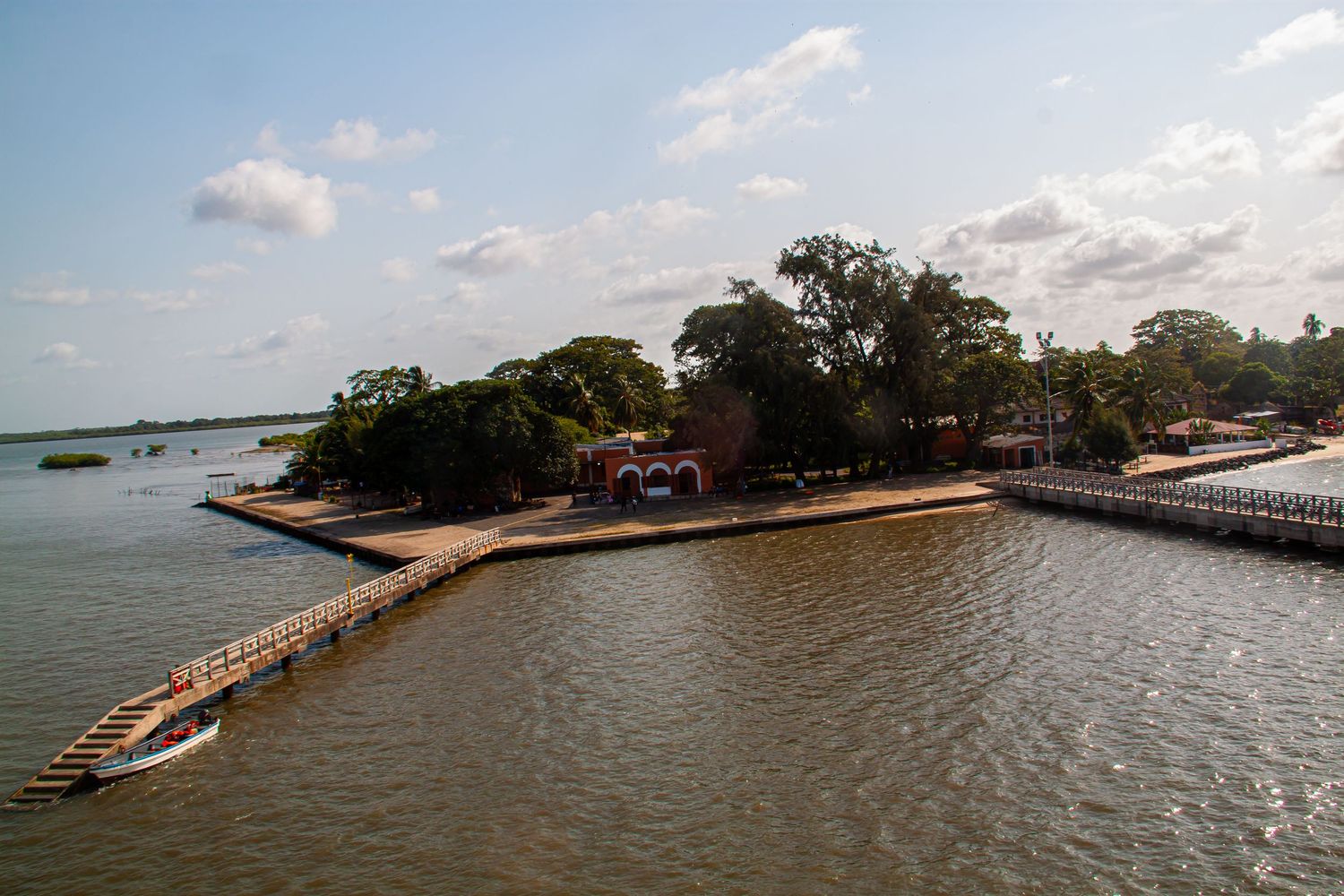 Aerial view of a small tropical island peninsula surrounded by calm waters with docks and red buildings.