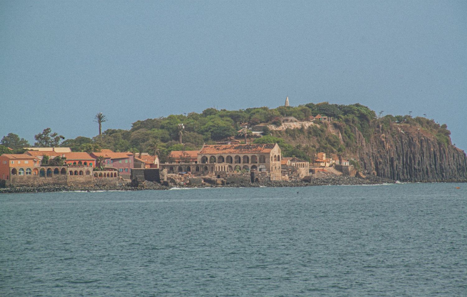 Historic island settlement with terracotta buildings nestled against rocky hillside viewed from the sea.