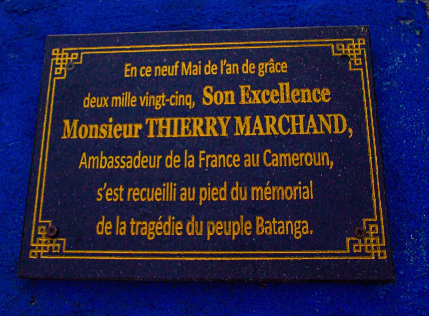 Blue memorial plaque in French honoring Ambassador Thierry Marchand at the Batanga tragedy memorial in Cameroon.