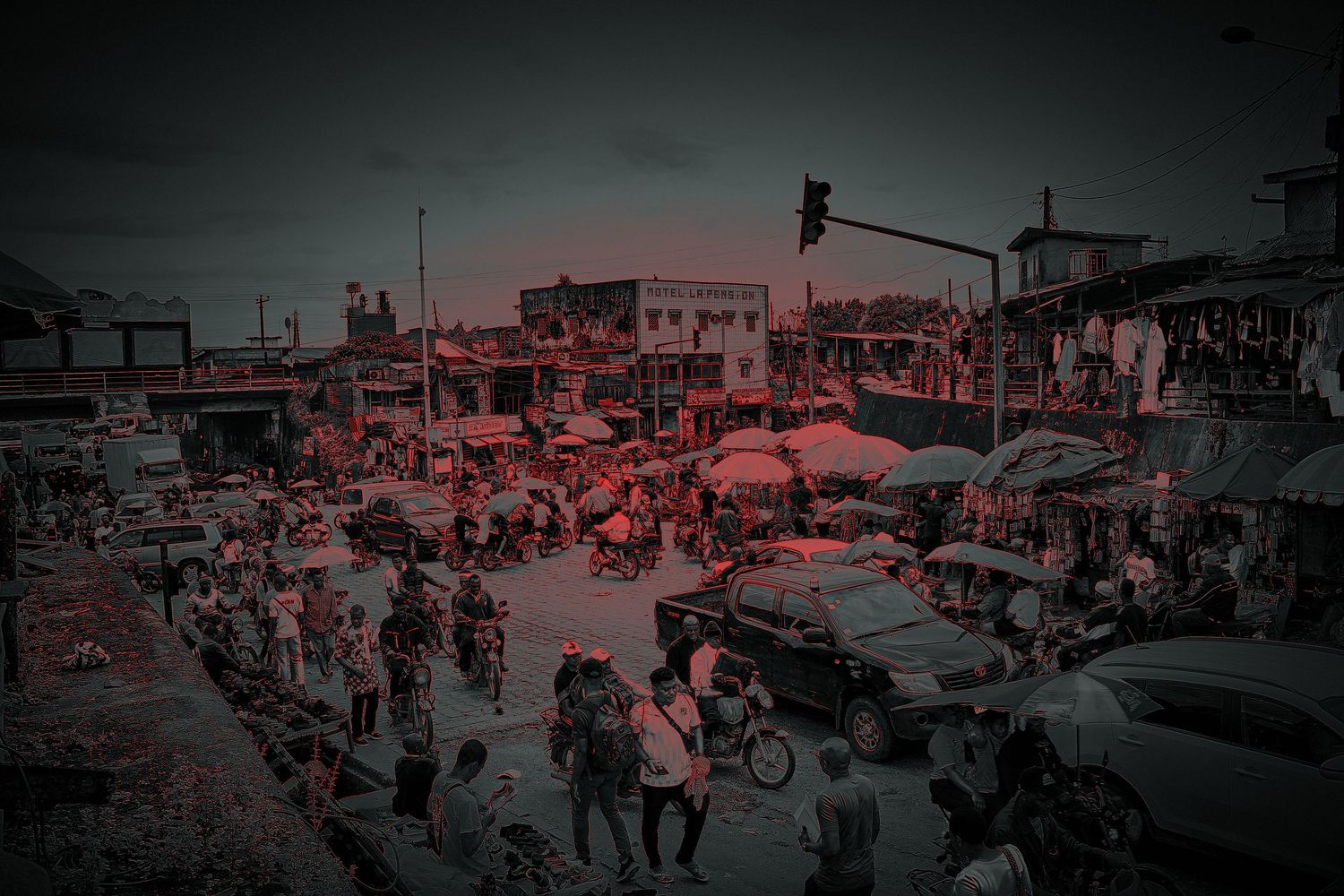 Crowded West African city market intersection with vendors, motorcycles and cars at sunset.