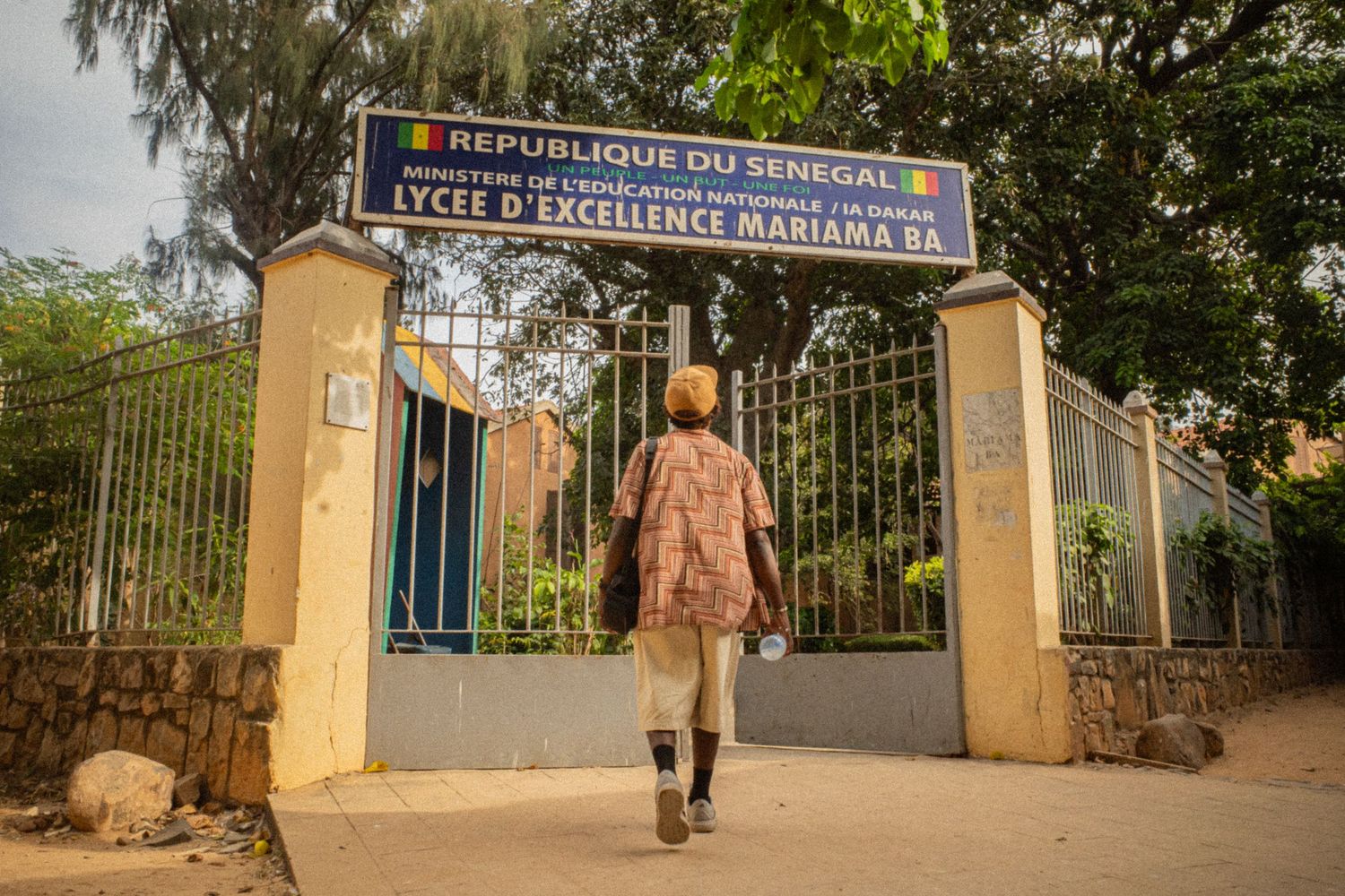 Person walking through the entrance gate of Lycee d Excellence Mariama Ba school in Senegal, West Africa.