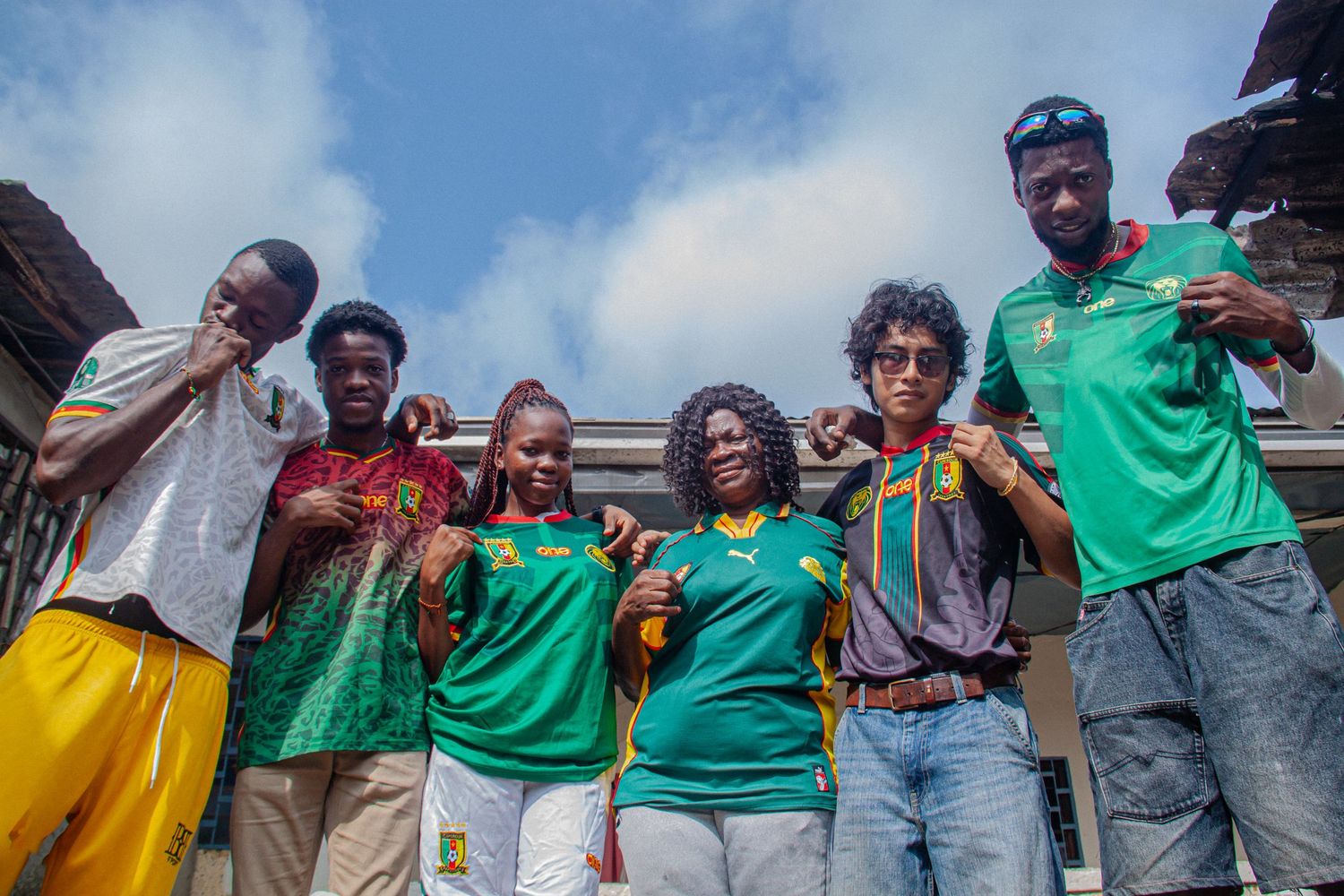 Group of six young African friends posing together wearing green Cameroon jerseys outdoors.