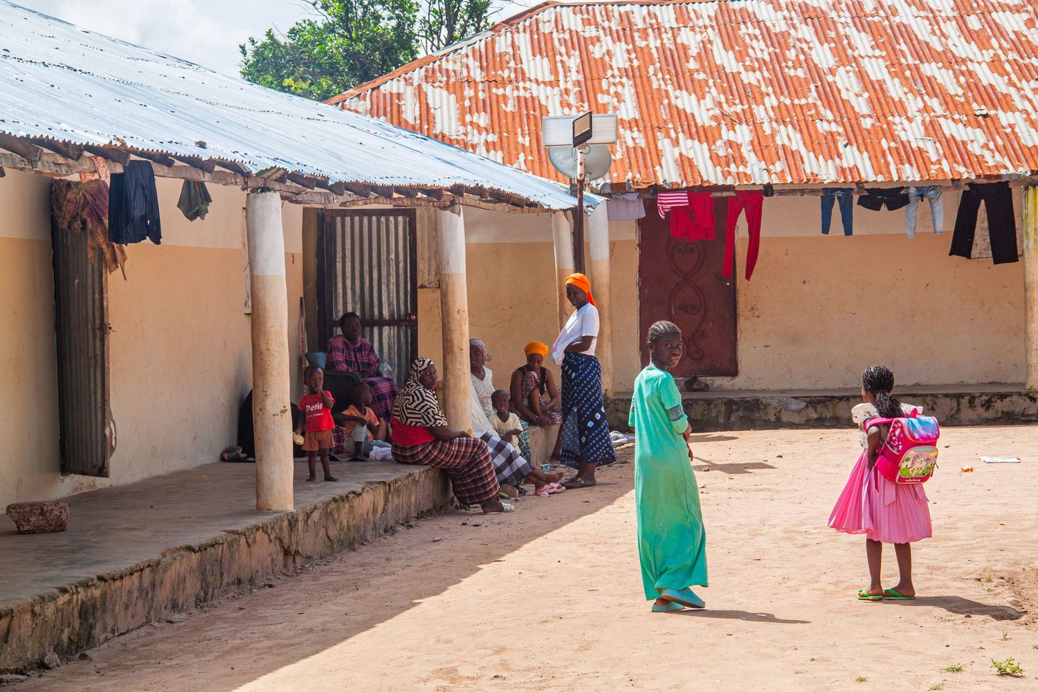 Women and children gather in a sandy courtyard between traditional mud-brick homes in West Africa.