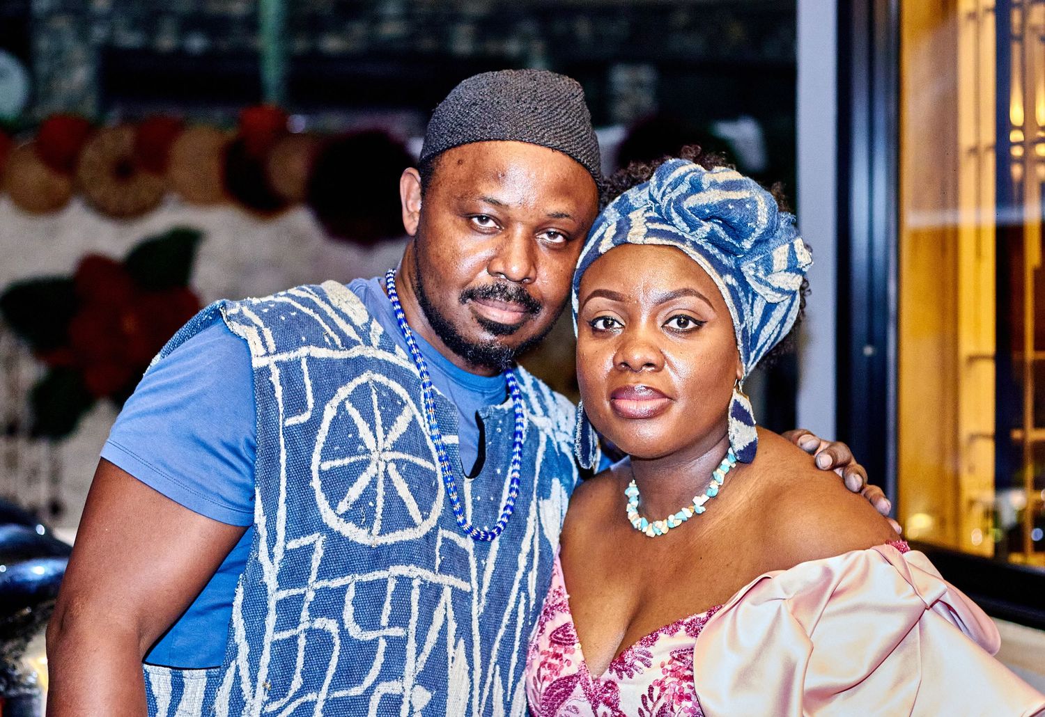 An African couple in traditional attire pose together affectionately at a decorated indoor venue.