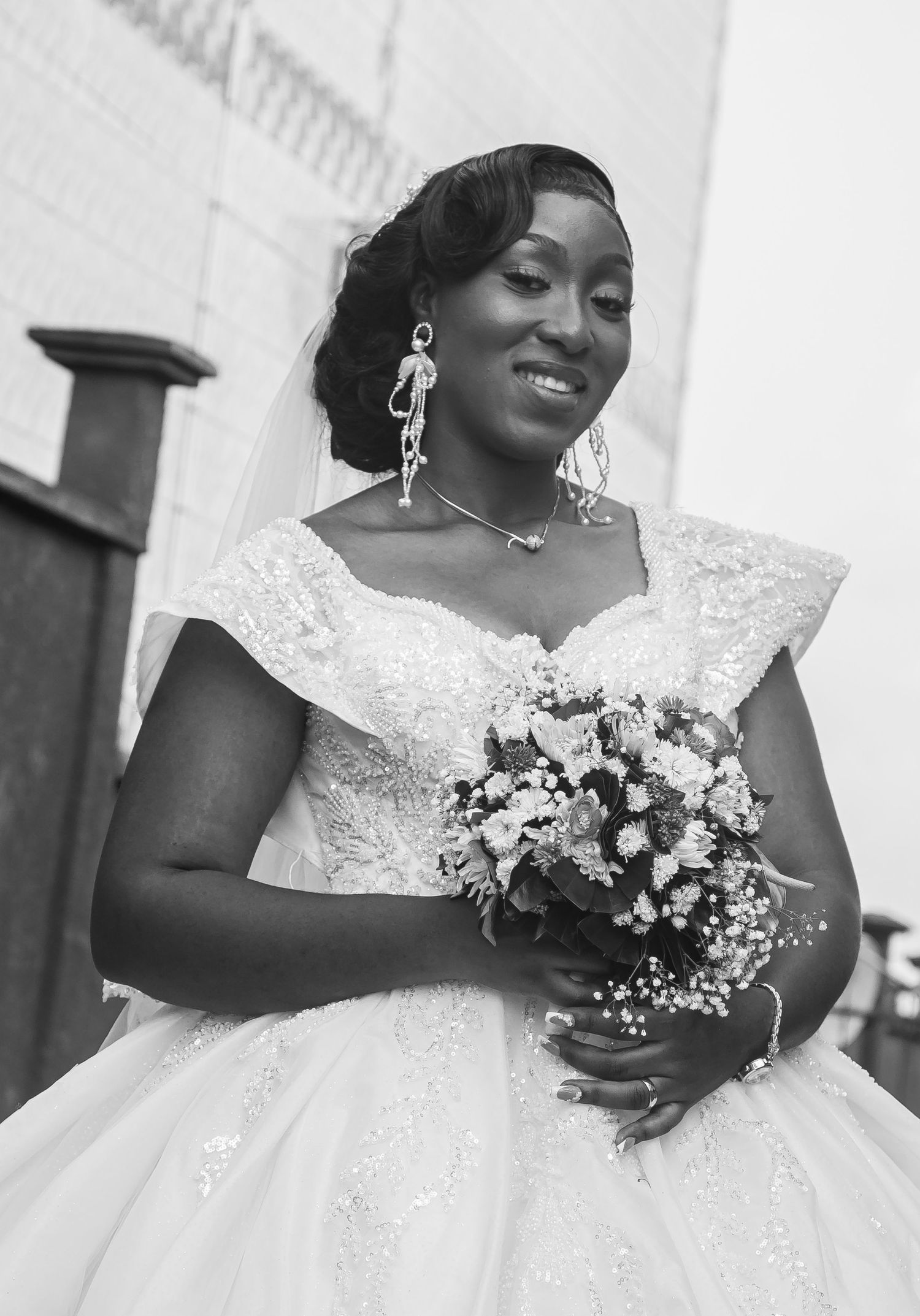 Beautiful African bride in a white lace wedding gown holding a floral bouquet, smiling.