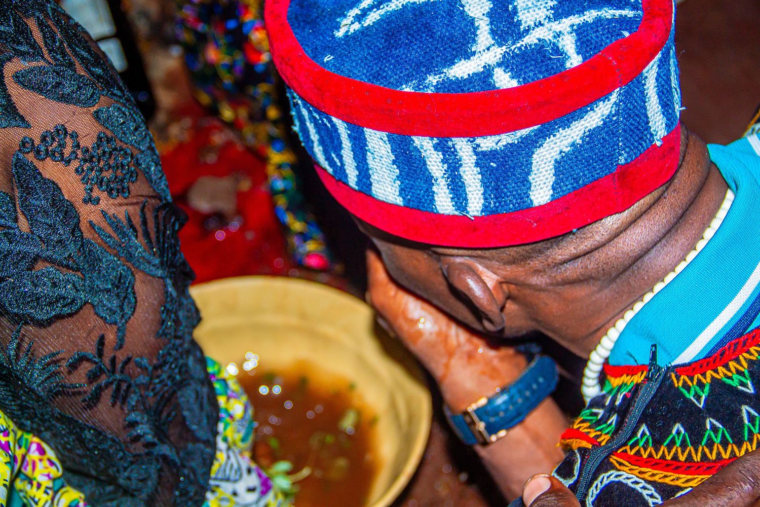 African man in traditional hat drinking from a bowl during a cultural ceremony ritual.
