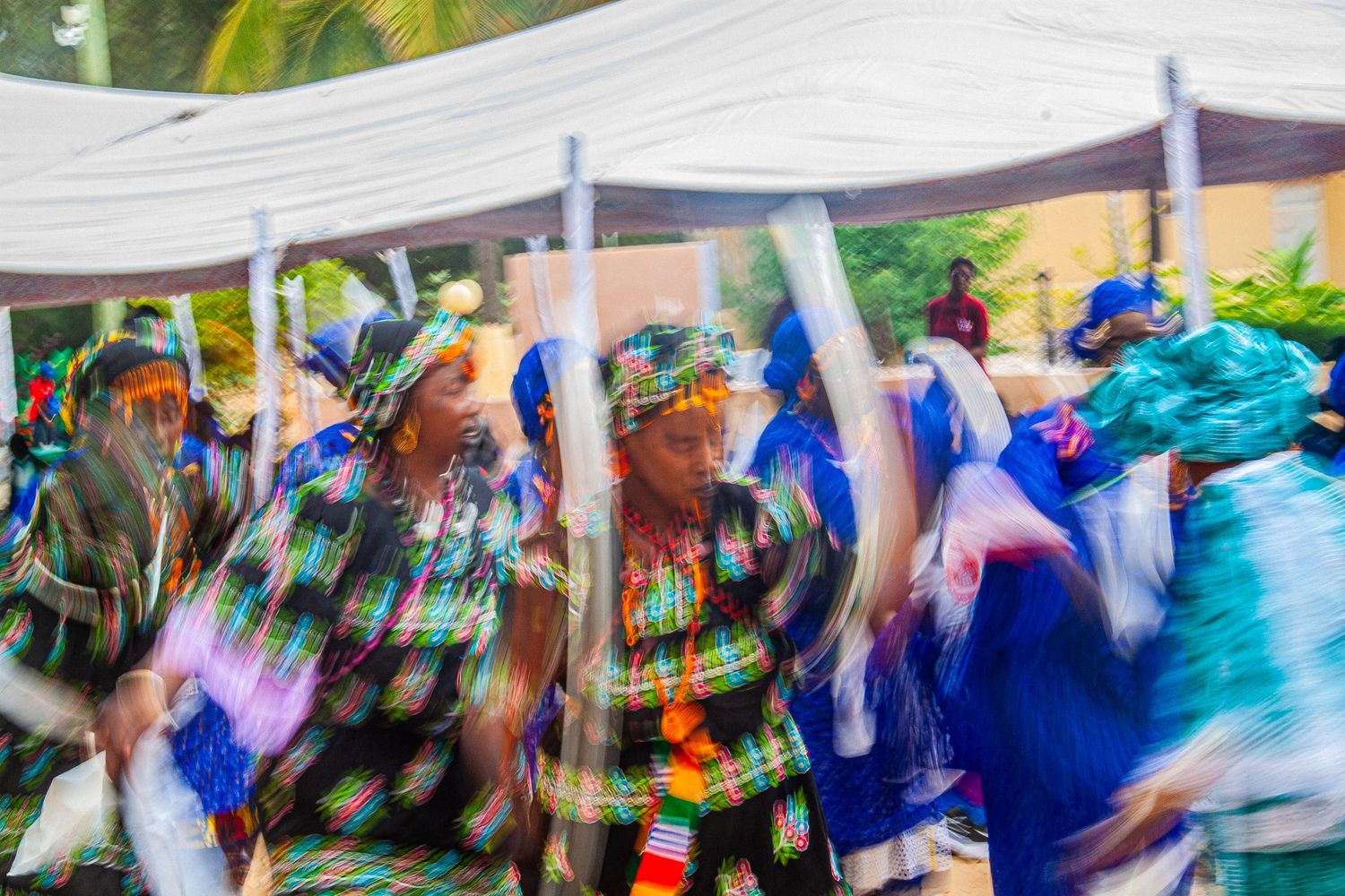 Blurred motion of women in colorful traditional African clothing dancing energetically at a festive gathering.