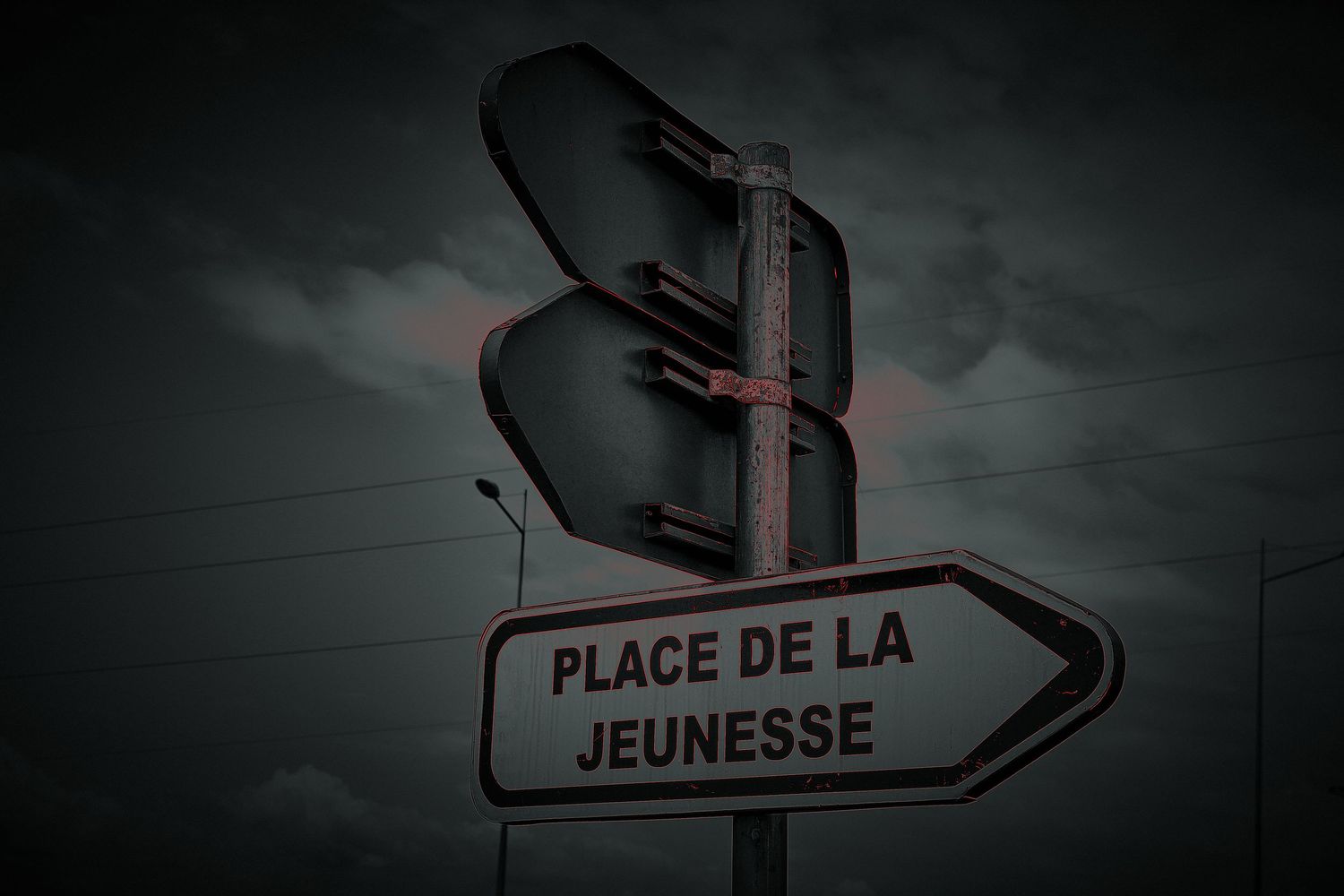 Street sign pointing to Place de la Jeunesse under a dark dramatic cloudy sky at night.