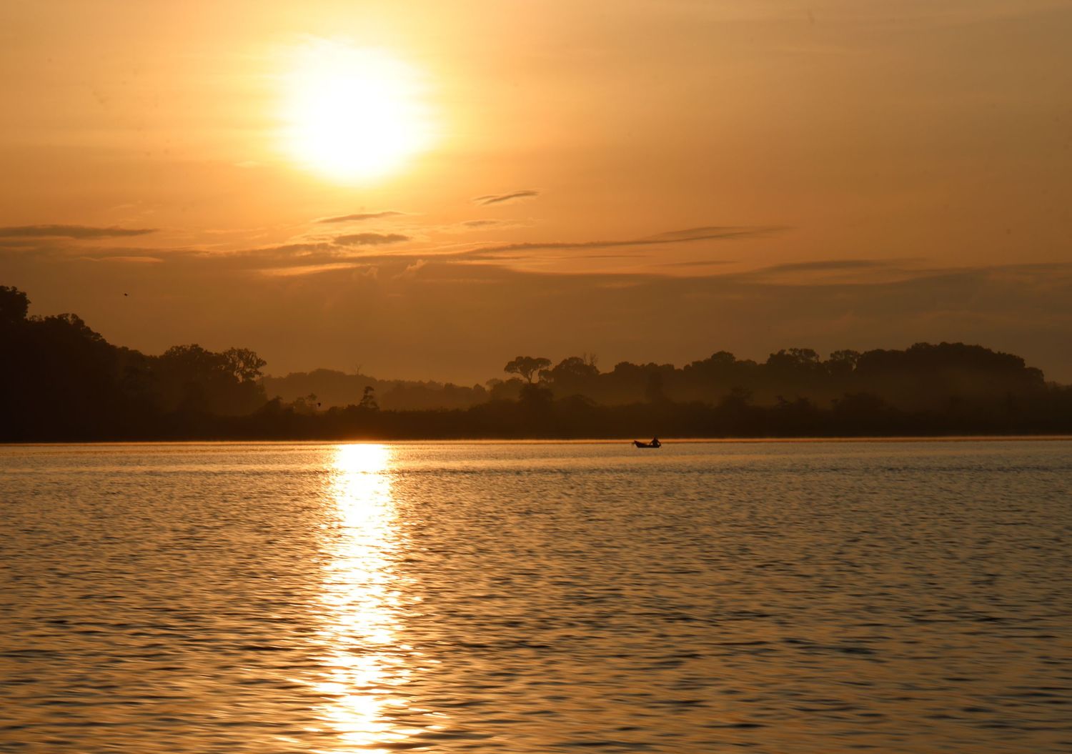 Golden sunset over a calm river with silhouetted trees and a small boat on the water.