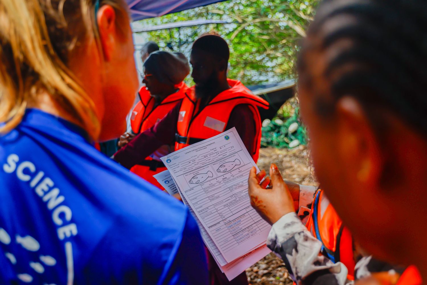 Researchers in orange life vests review scientific data forms during an outdoor conservation fieldwork session.