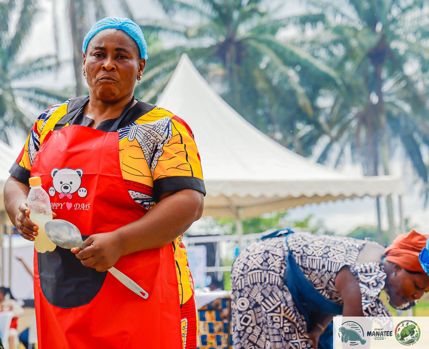 Woman in red apron cooking at outdoor food preparation community event.