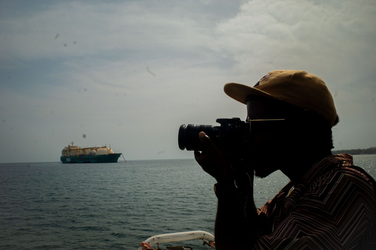 Silhouette of photographer capturing cargo ship on open ocean from shoreline.