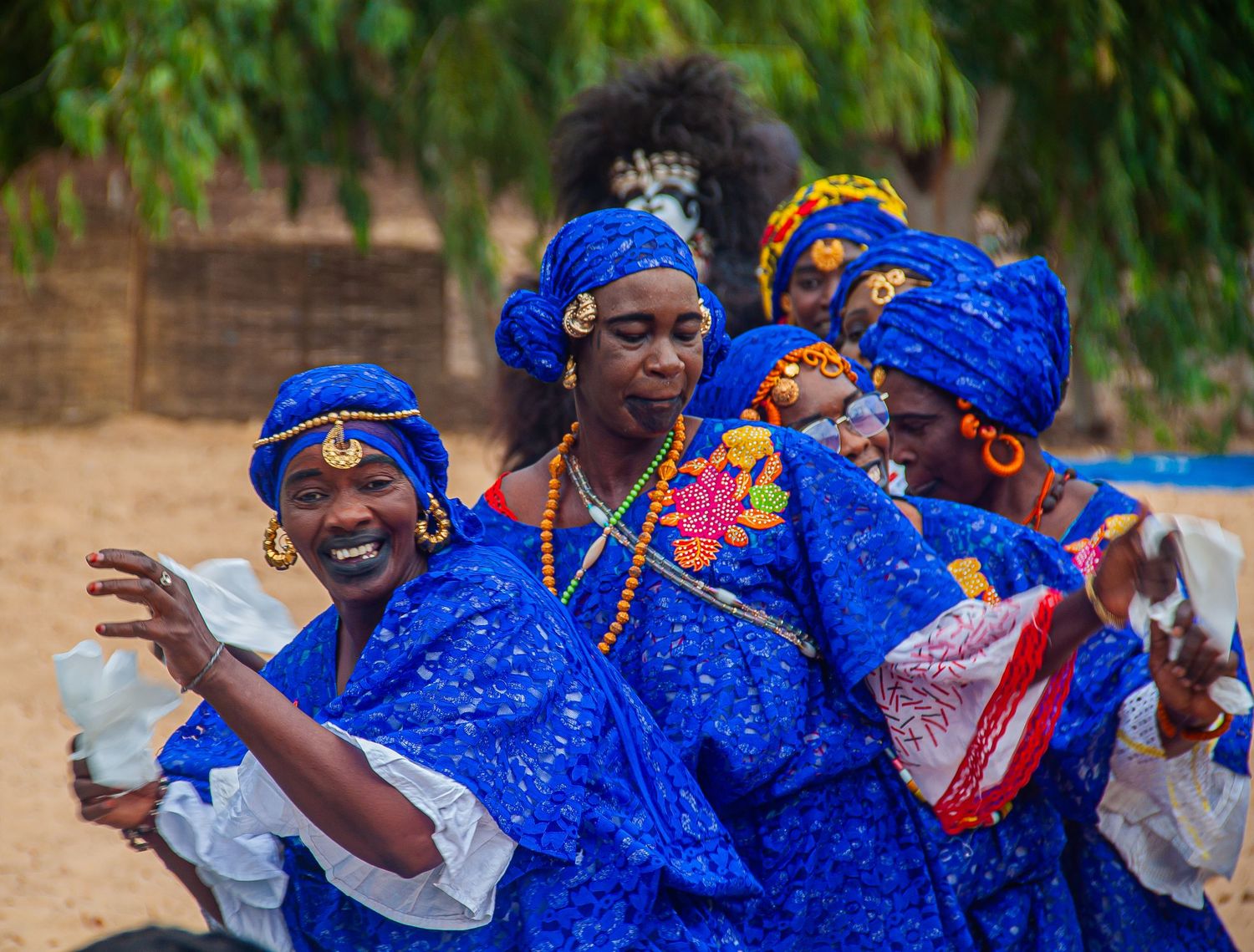 Women in vibrant blue traditional African attire dance joyfully at a cultural celebration.