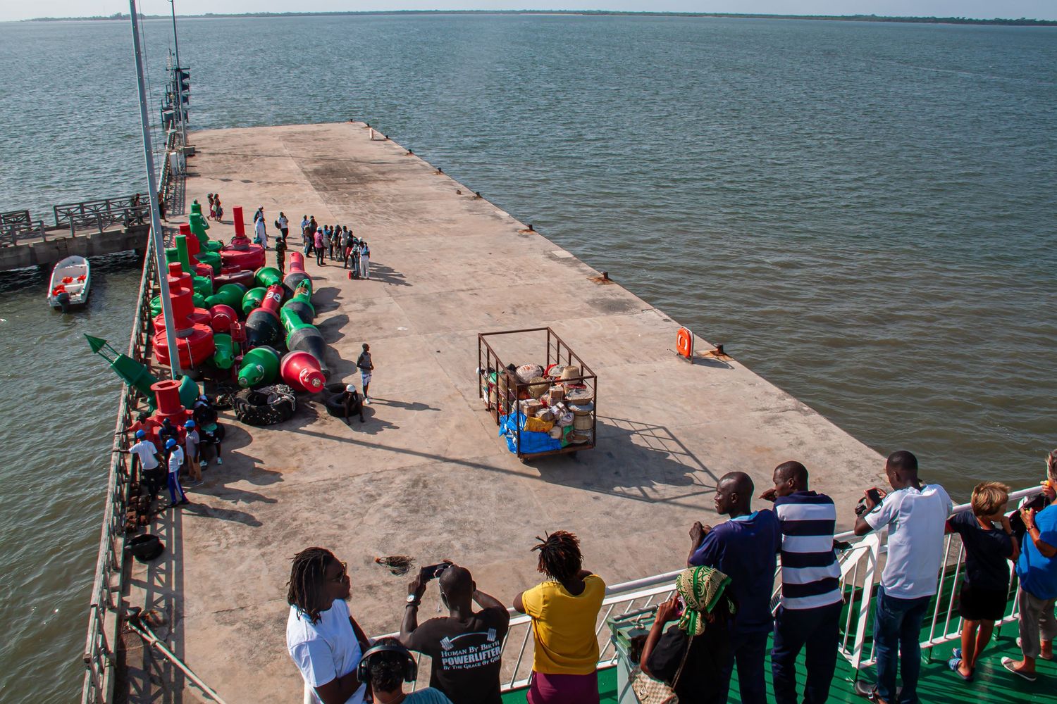 Aerial view of a concrete pier with colorful crowds gathered on a dock in West Africa.