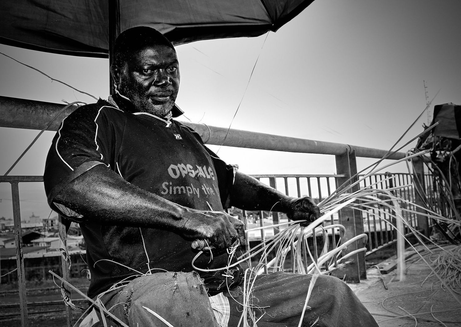 Black and white photo of an African man weaving basket crafts outdoors.