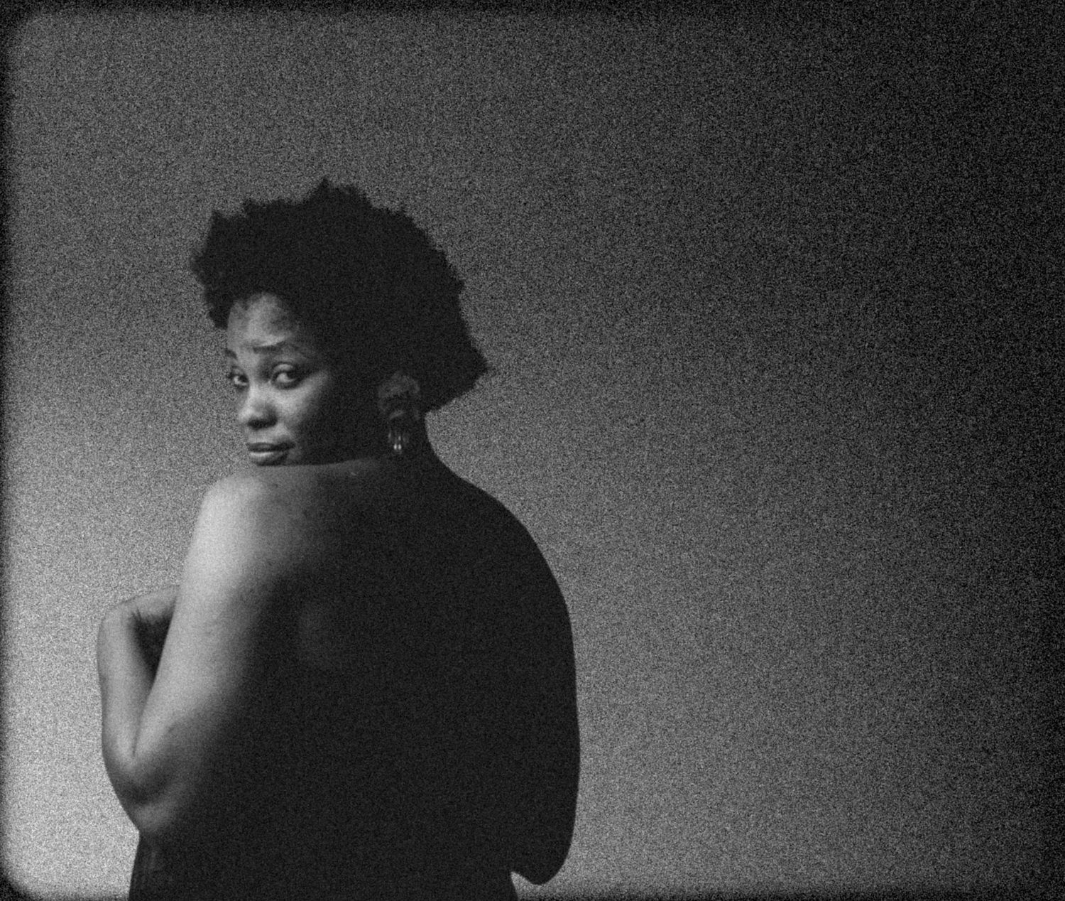 Grainy black and white portrait of woman with short natural hair looking over bare shoulder.