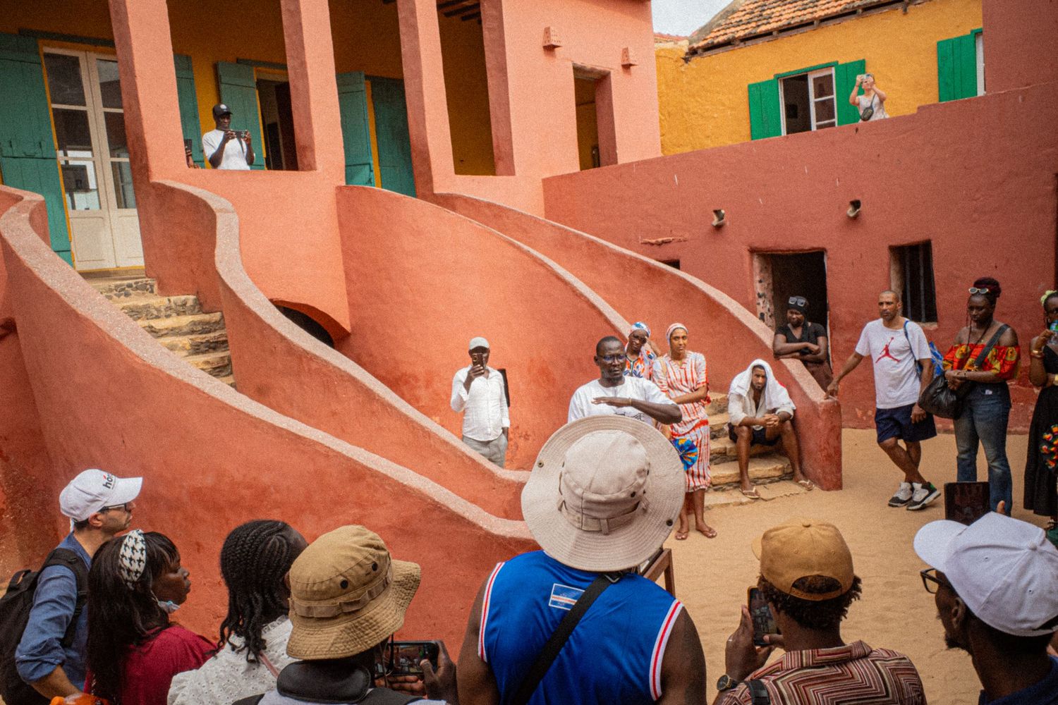 Tourists gather in the courtyard of a vibrant red colonial building on Goree Island, Senegal.