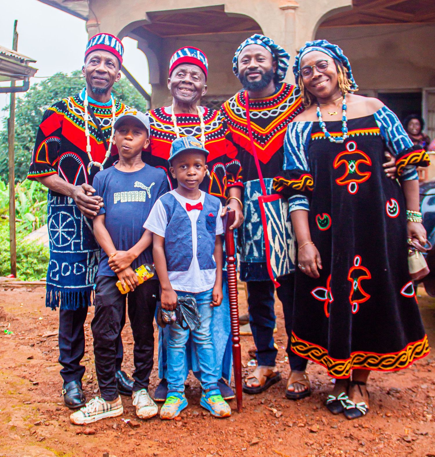 Family group in vibrant traditional Cameroonian Ndop attire posing together at an outdoor cultural event.