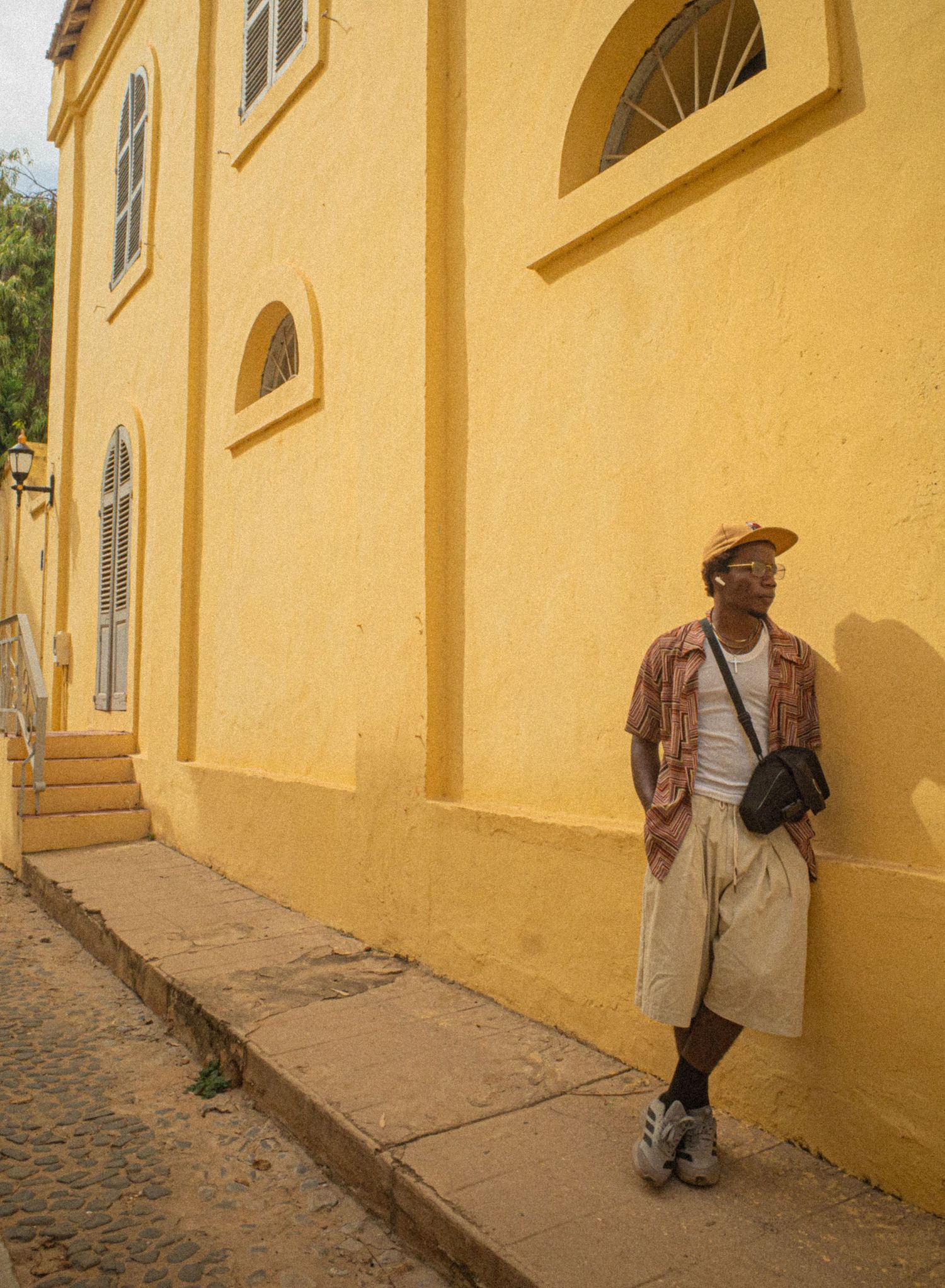 A man leans against a vibrant yellow colonial building on a cobblestone street in Goree Island, Senegal.